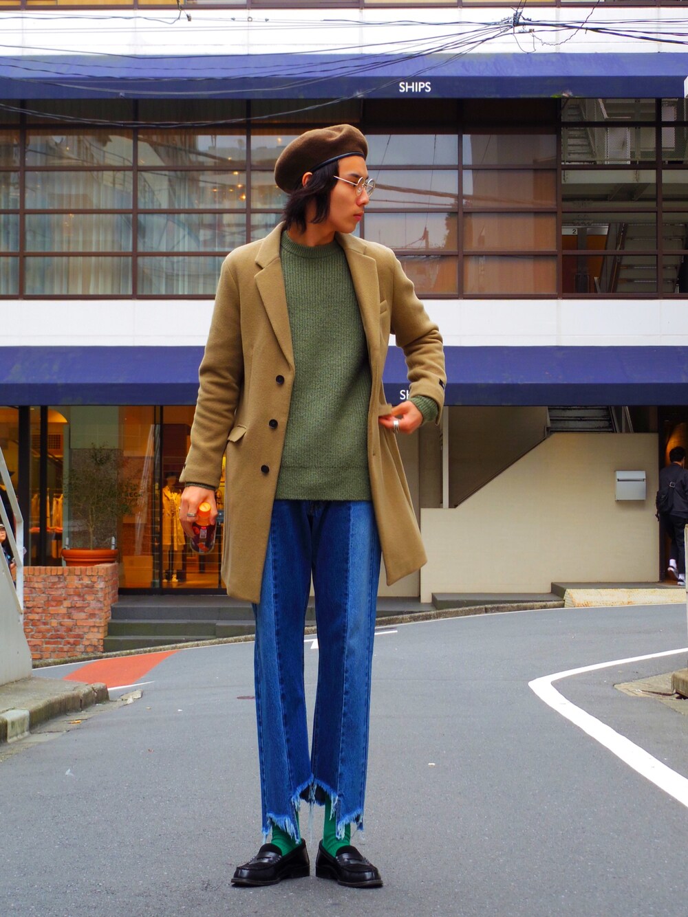 ベージュ系のチェスターコート、グリーン系のニット/セーター、ブルー系のデニムパンツを着用したメンズの秋コーディネートの1枚目の写真