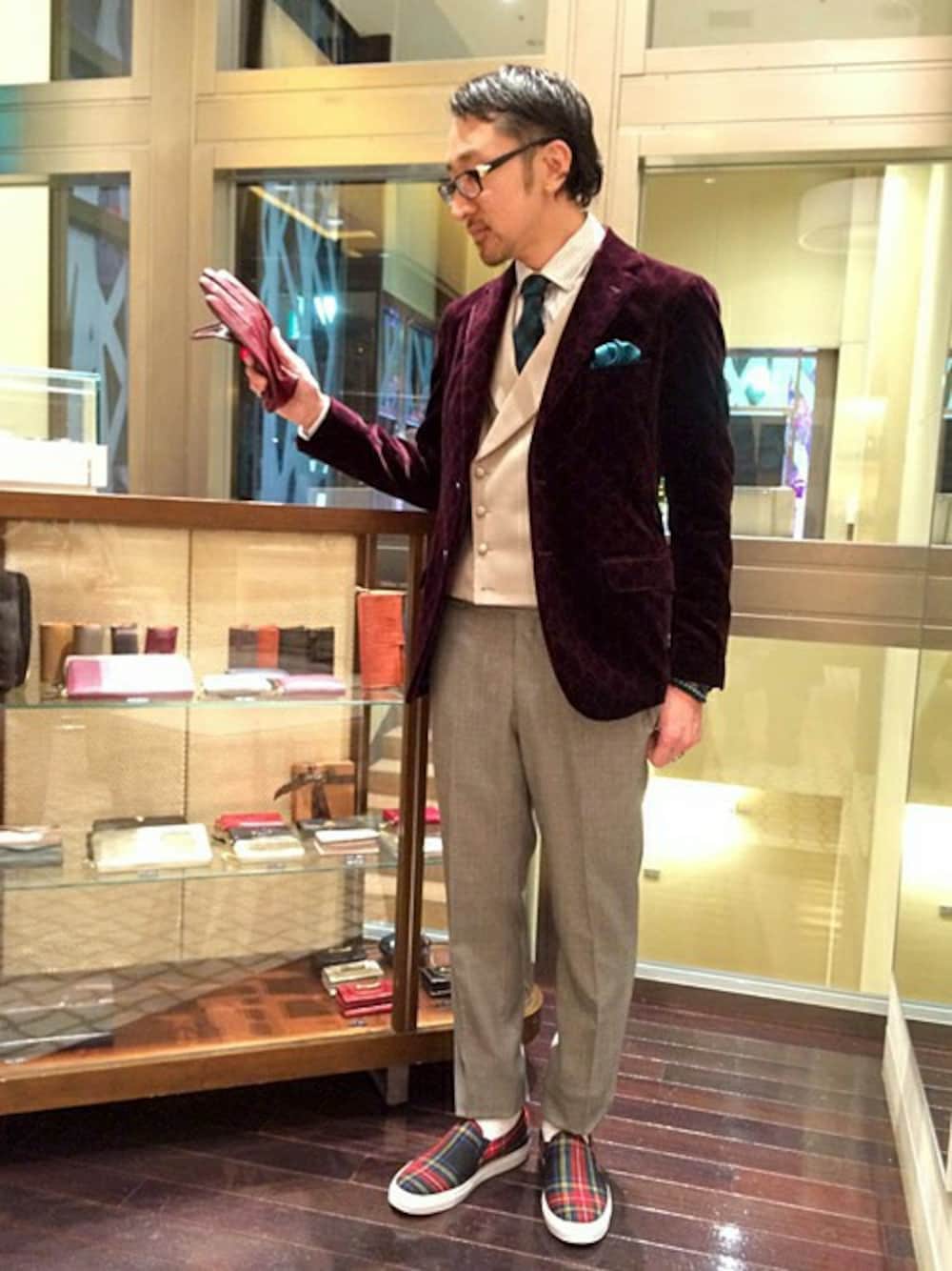 レッド系のテーラードジャケット、グリーン系のネクタイ、レッド系の手袋を着用したメンズの冬コーディネートの1枚目の写真