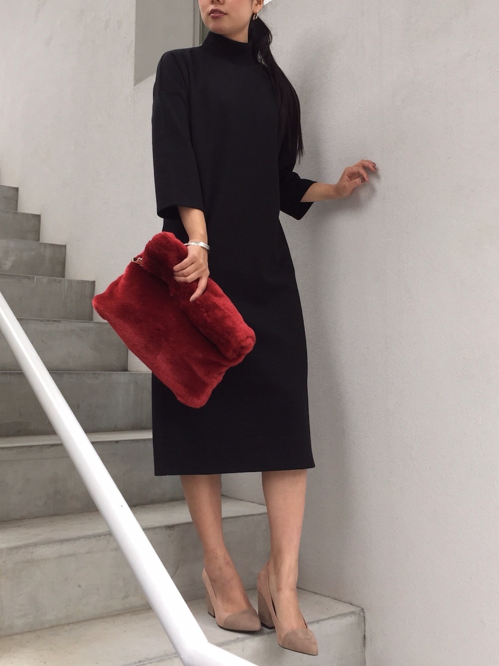 レッド系のクラッチバッグ、ブラック系のワンピース、ベージュ系のパンプスを着用したレディースの秋コーディネートの1枚目の写真