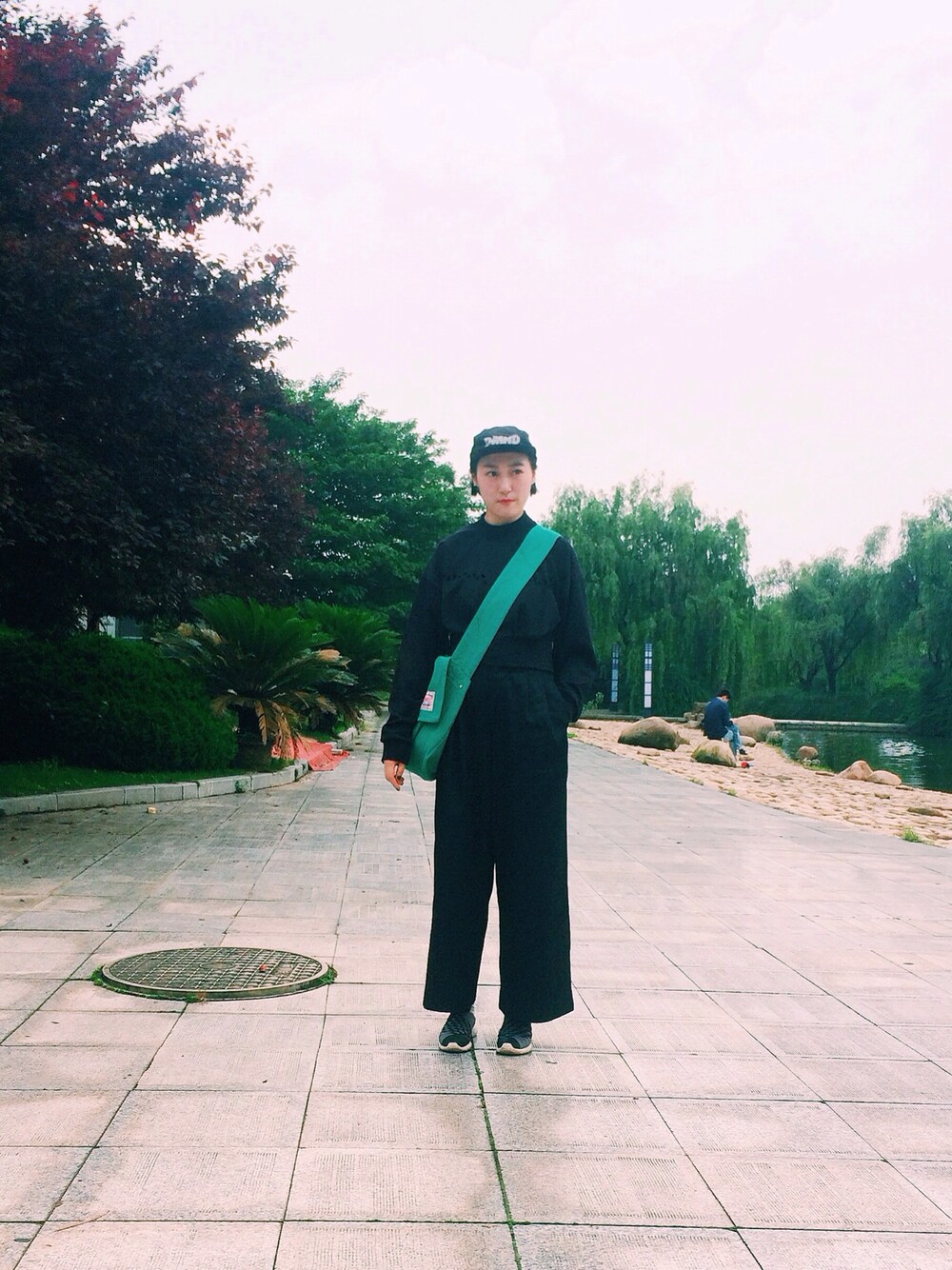 グリーン系のメッセンジャーバッグ、ブラック系のデニムパンツ、ブラック系のスニーカーを着用したレディースの夏コーディネートの1枚目の写真