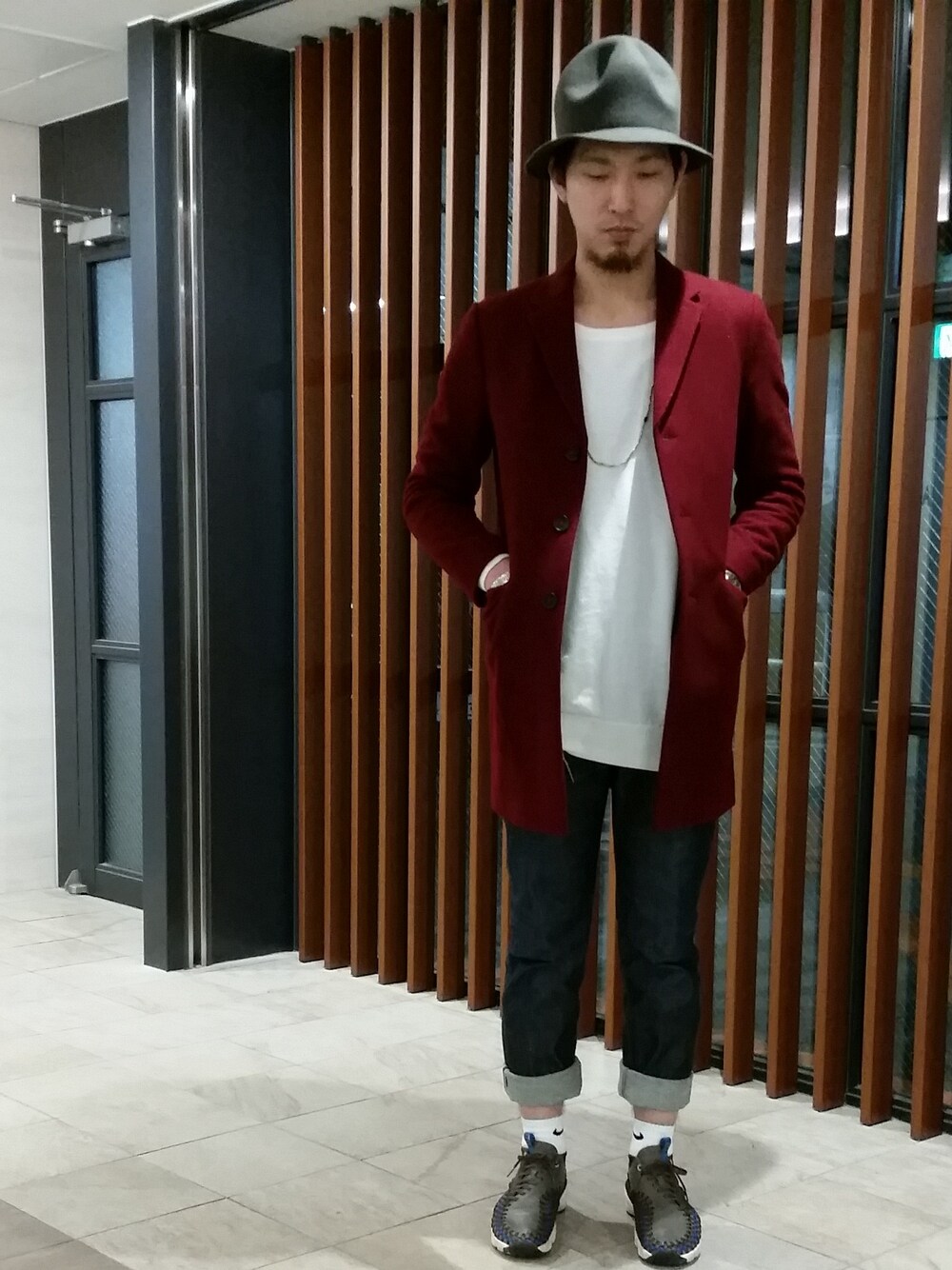 レッド系のチェスターコート、ホワイト系のニット/セーター、ブルー系のデニムパンツを着用したメンズの冬コーディネートの1枚目の写真