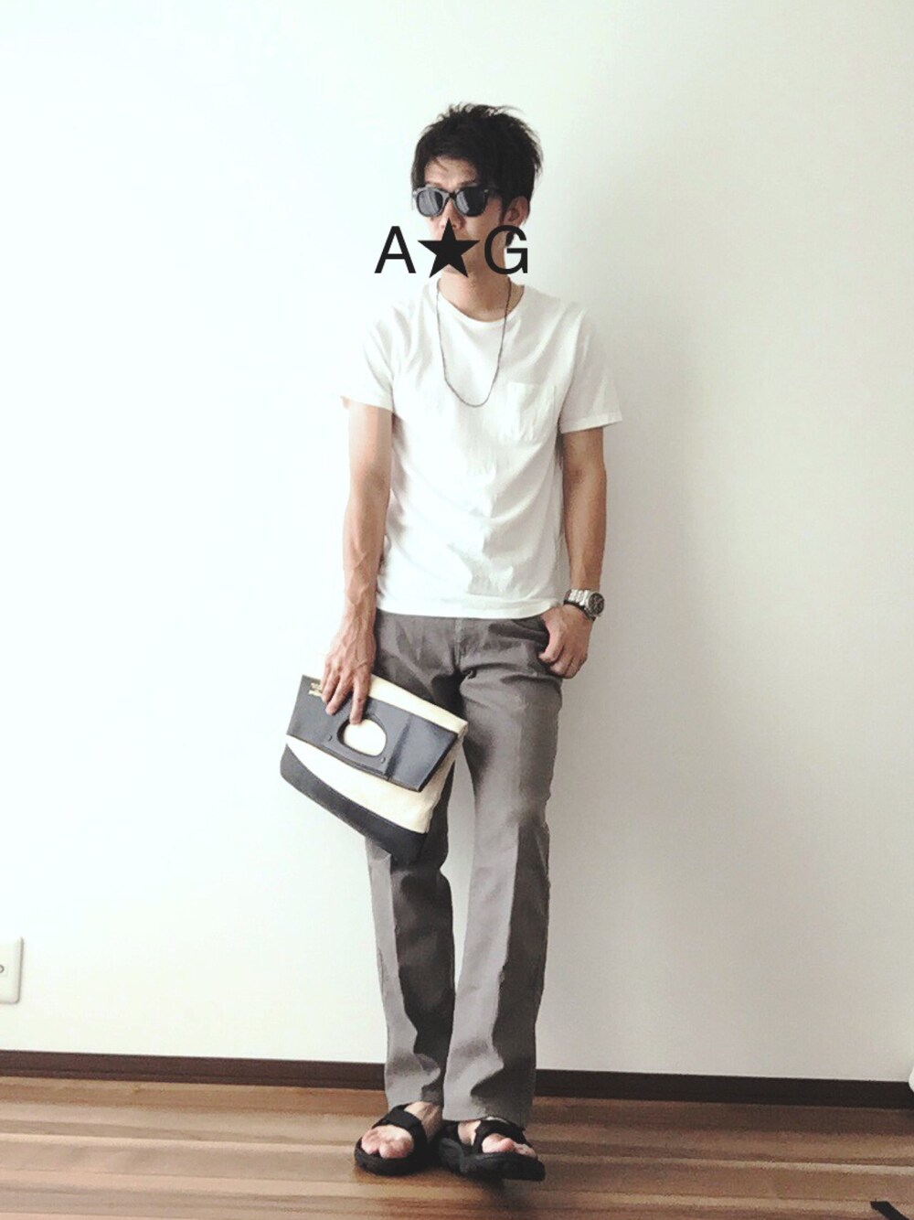 ホワイト系のクラッチバッグ、ホワイト系のTシャツ/カットソー、グレー系のスラックスを着用したメンズの夏コーディネートの1枚目の写真