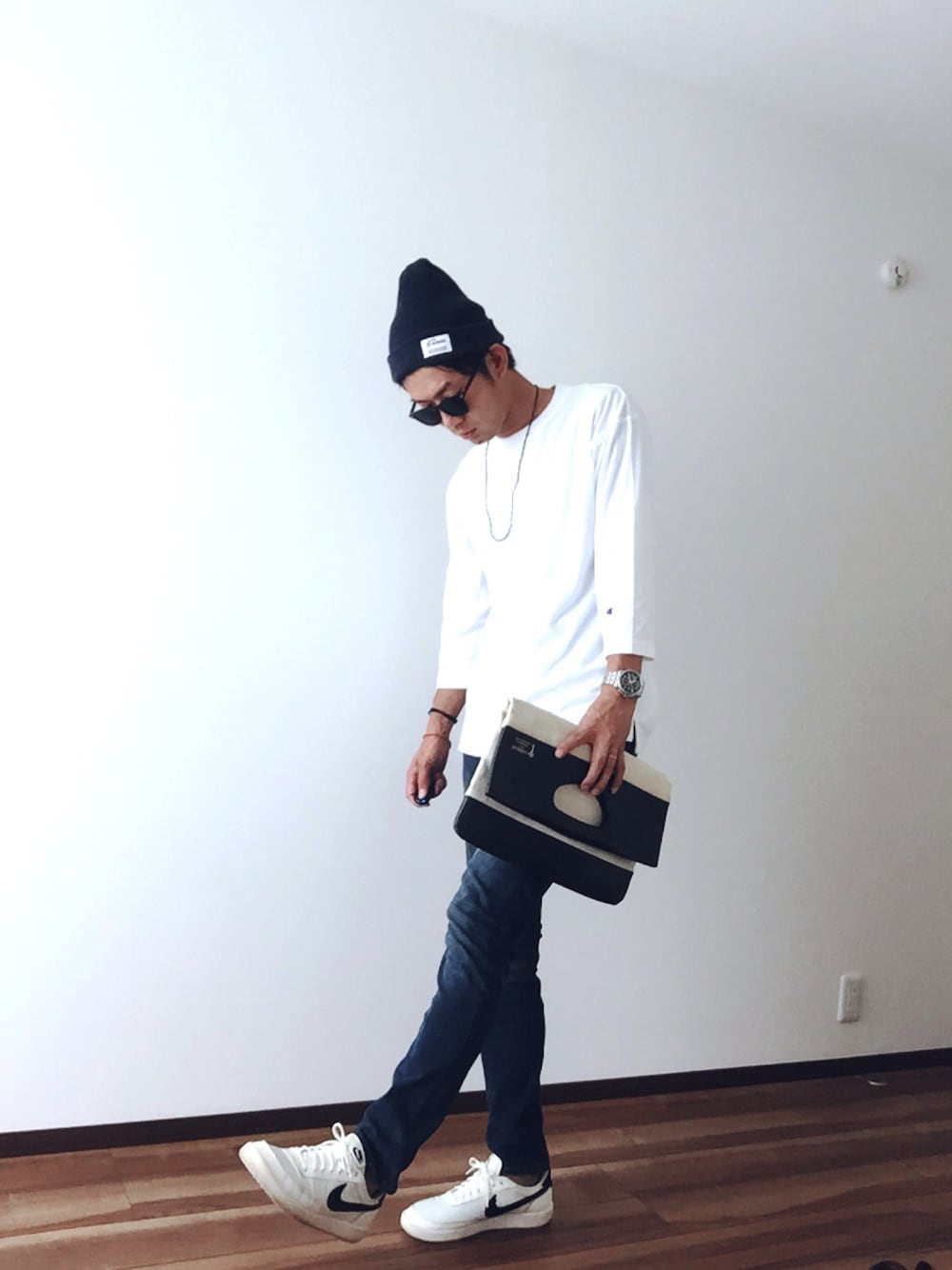 ホワイト系のTシャツ/カットソー、ホワイト系のクラッチバッグ、ブルー系のデニムパンツを着用したメンズの秋コーディネートの1枚目の写真