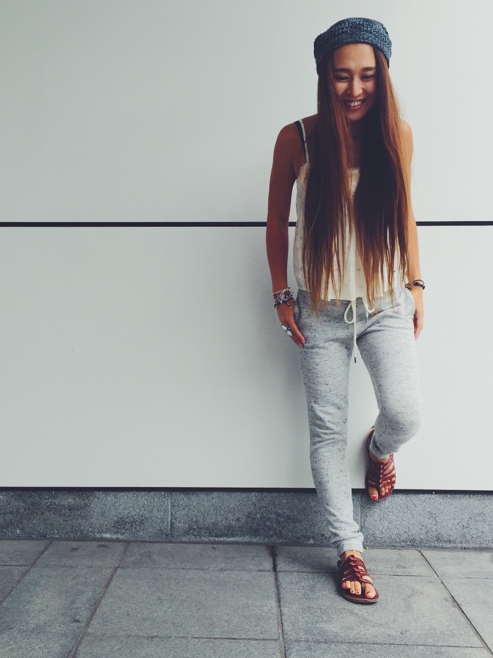 ホワイト系のキャミソール、グレー系のパンツ、ブラック系のハットを着用したレディースの夏コーディネートの1枚目の写真