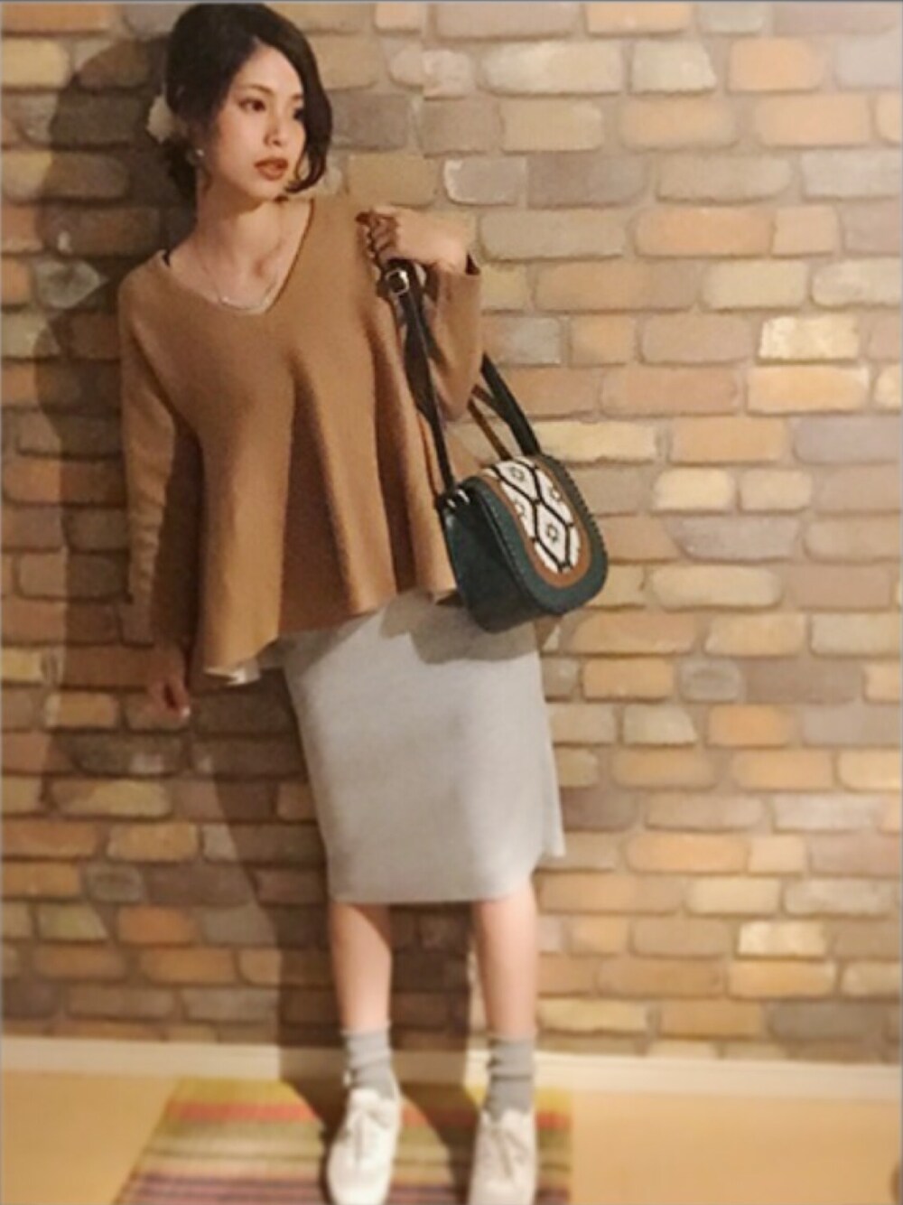 ベージュ系のニット/セーター、グレー系のスカート、ホワイト系のスニーカーを着用したレディースの秋コーディネートの1枚目の写真