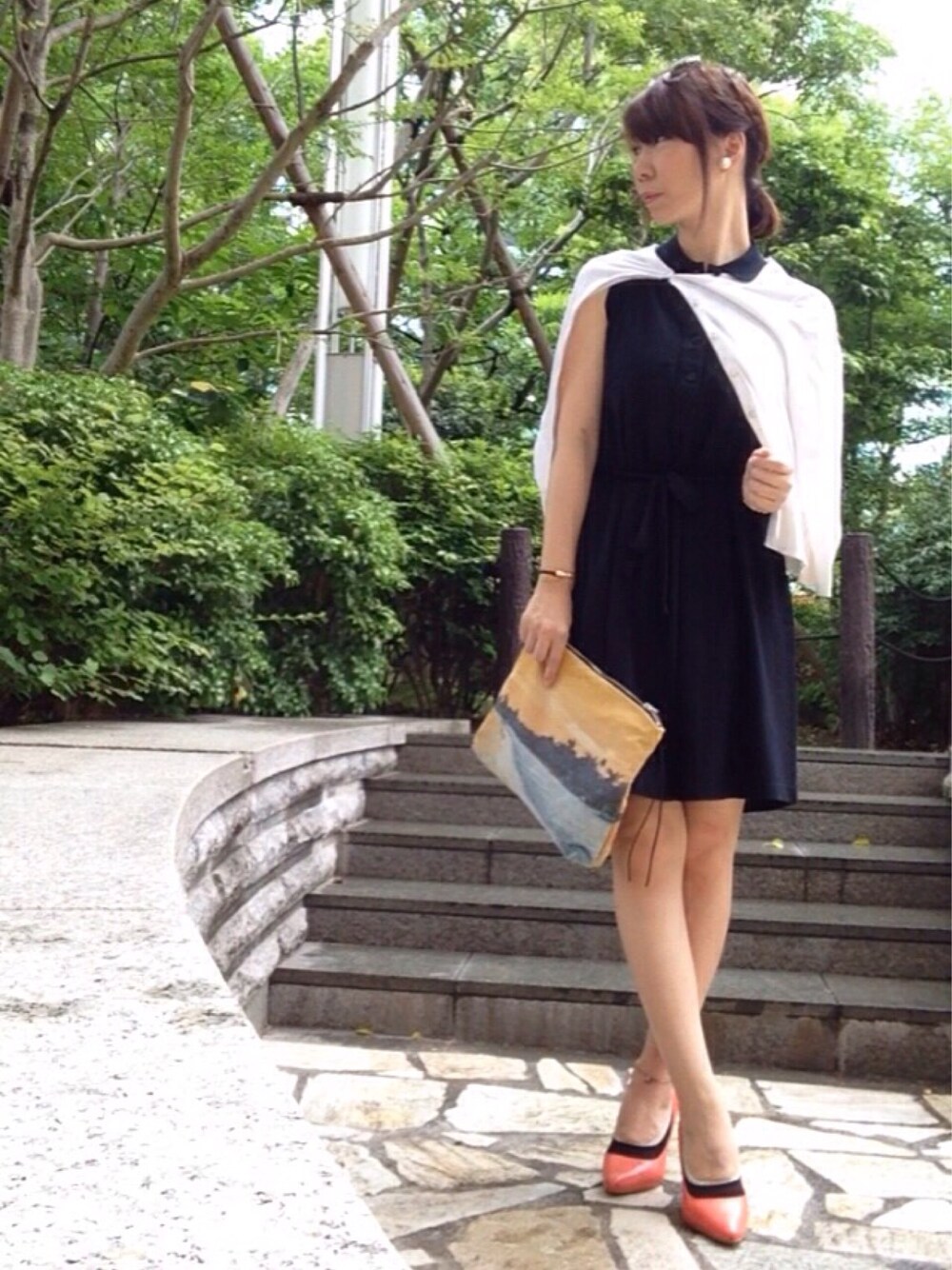 ブラック系のワンピース、ホワイト系のカーディガン/ボレロ、オレンジ系のクラッチバッグを着用したレディースの夏コーディネートの1枚目の写真