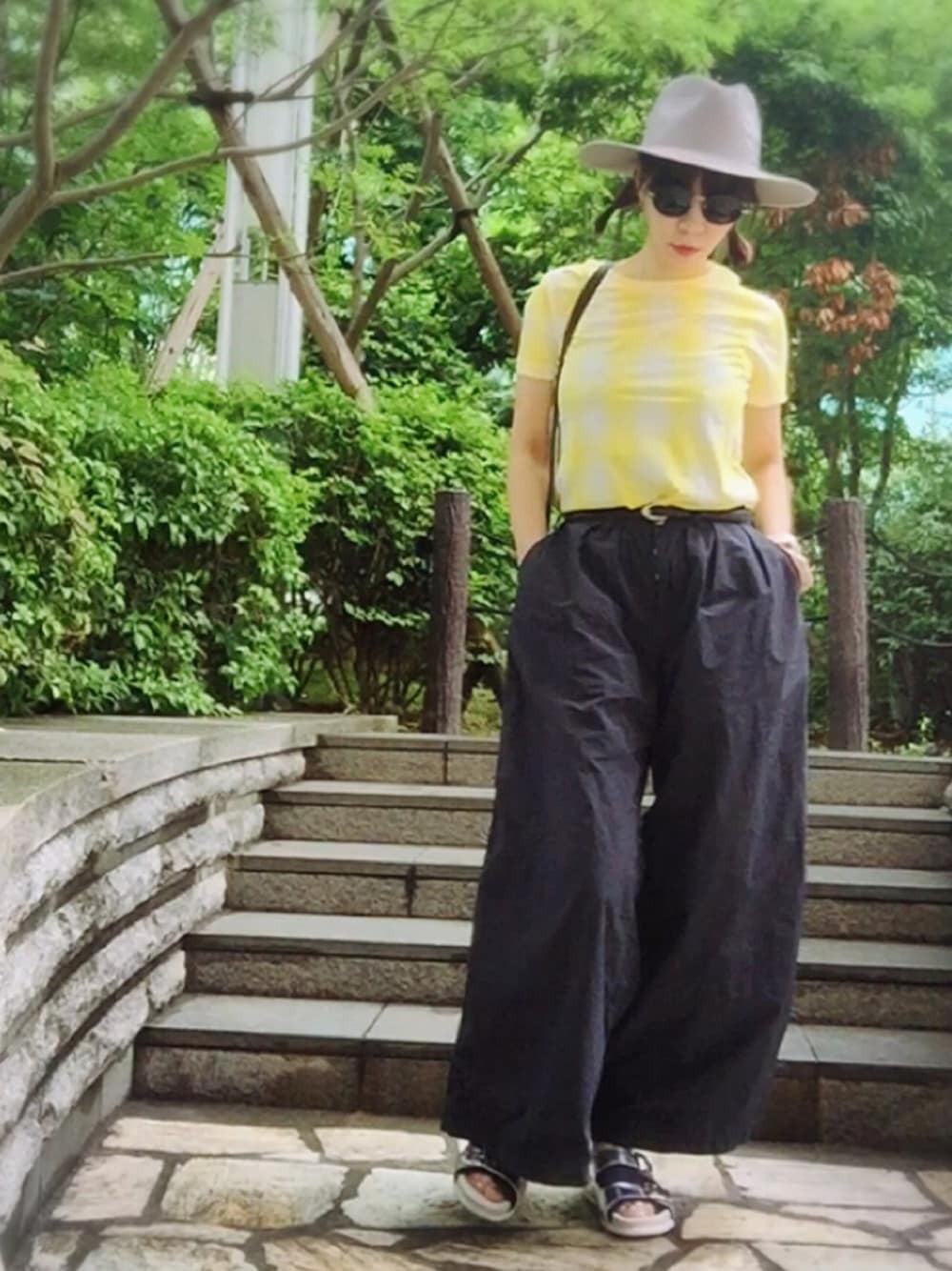 イエロー系のトップス、ブラック系のパンツ、シルバー系のサンダルを着用したレディースの夏コーディネートの1枚目の写真