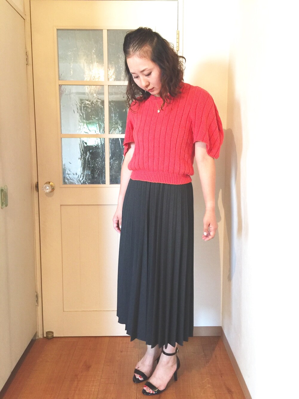 グレー系のスカート、ブラック系のパンプス、オレンジ系のニット/セーターを着用したレディースの秋コーディネートの1枚目の写真