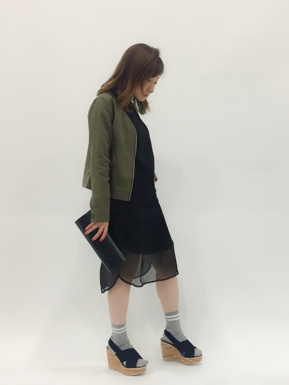 ブラック系のワンピース、グリーン系のノーカラージャケット、ブラック系のクラッチバッグを着用したレディースの春コーディネートの1枚目の写真