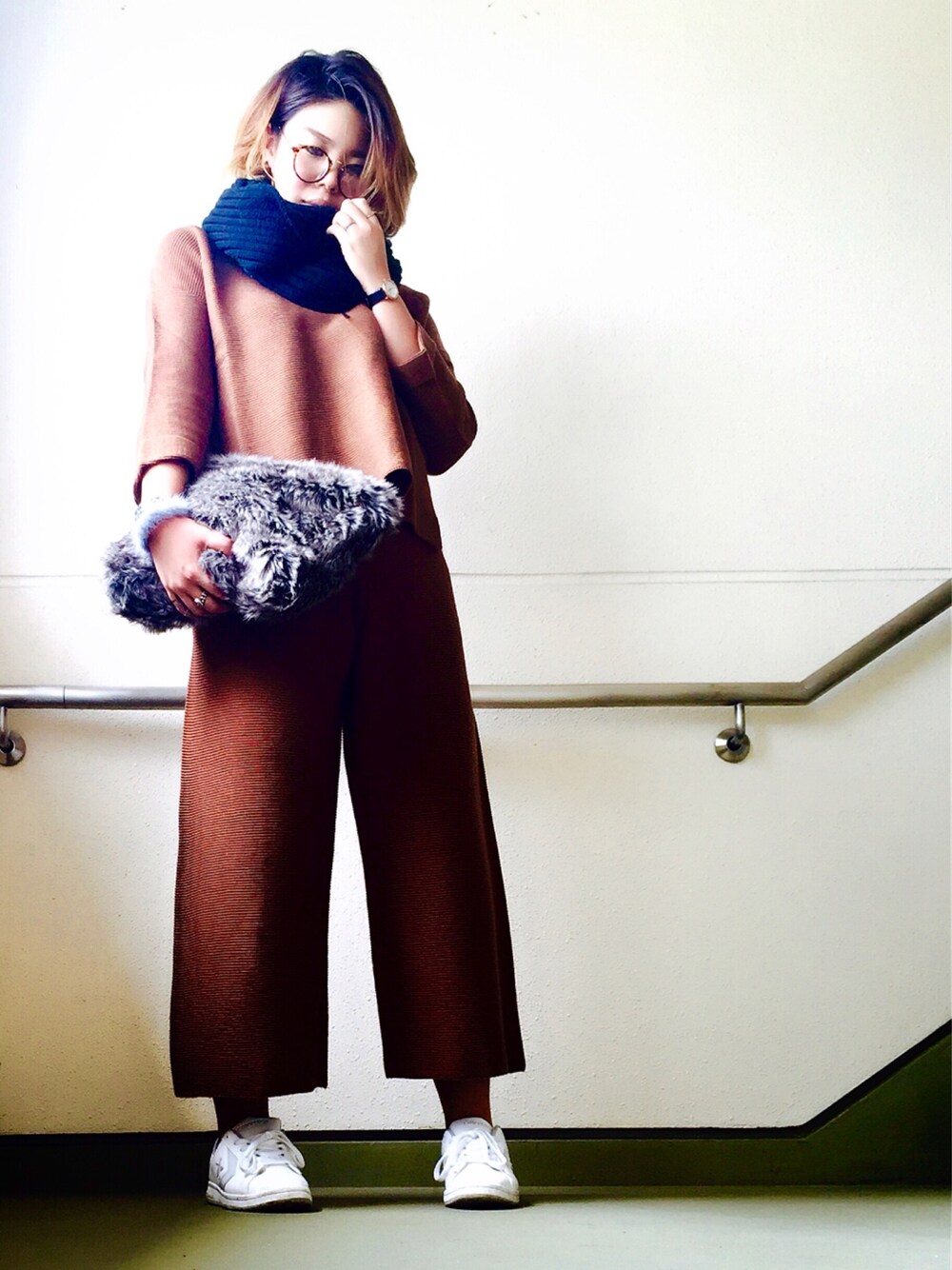 グレー系のクラッチバッグ、ブラウン系のニット/セーター、ホワイト系のスニーカーを着用したレディースの秋コーディネートの1枚目の写真