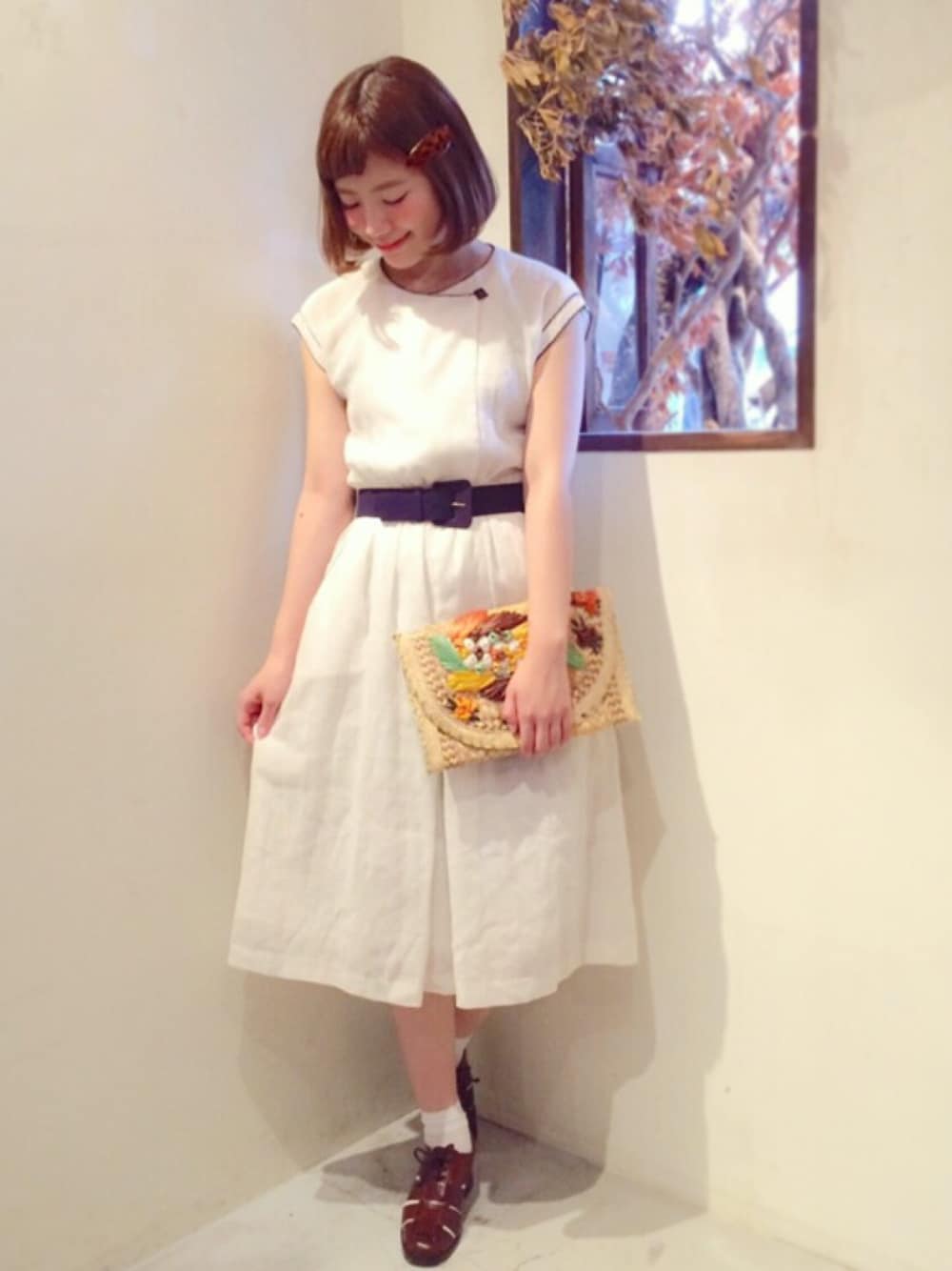 ホワイト系のワンピース、イエロー系のクラッチバッグ、ブラウン系のドレスシューズを着用したレディースの夏コーディネートの1枚目の写真