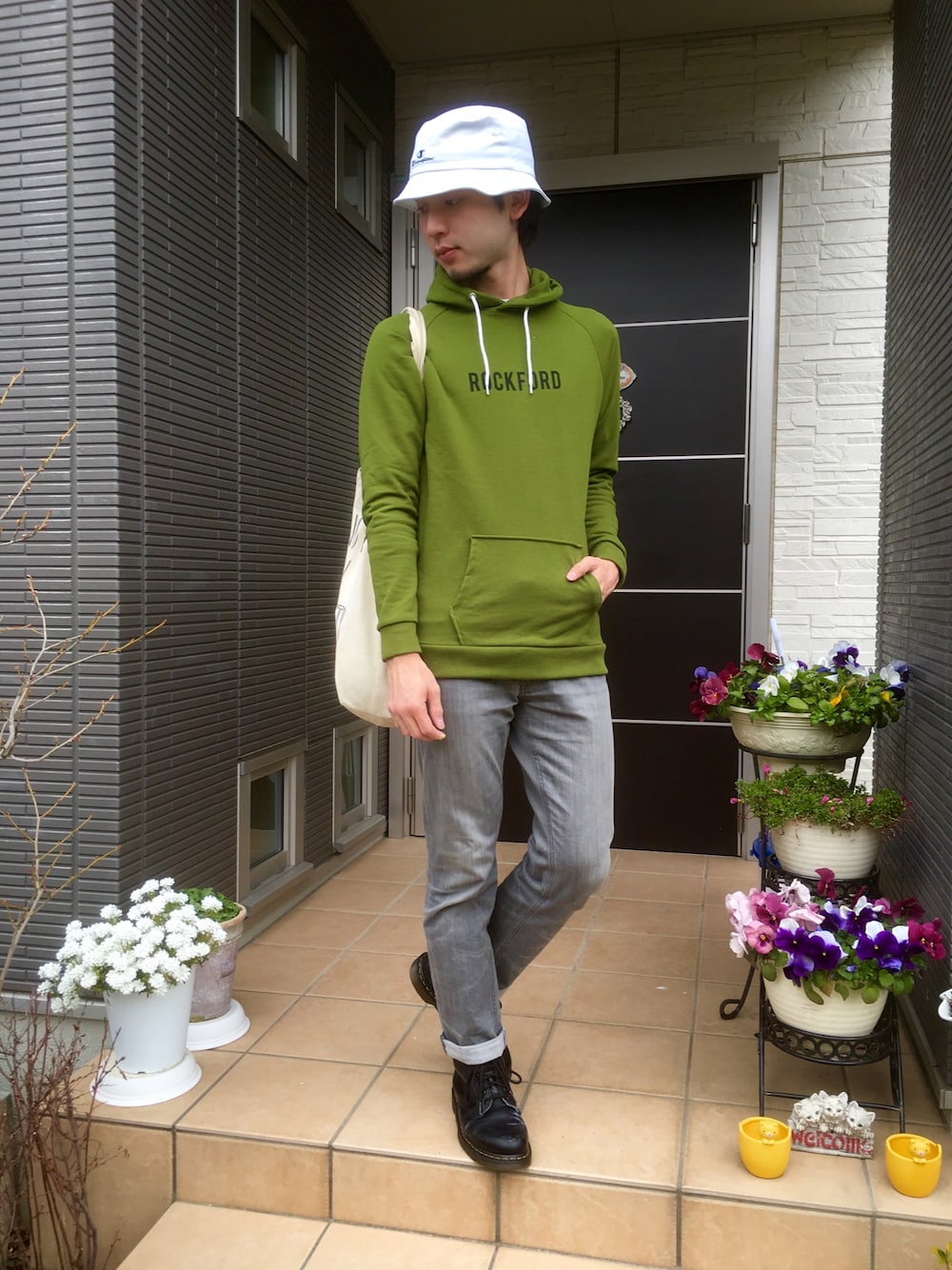 グレー系のデニムパンツ、ブラック系のブーツ、ホワイト系のトートバッグを着用したメンズの春コーディネートの1枚目の写真