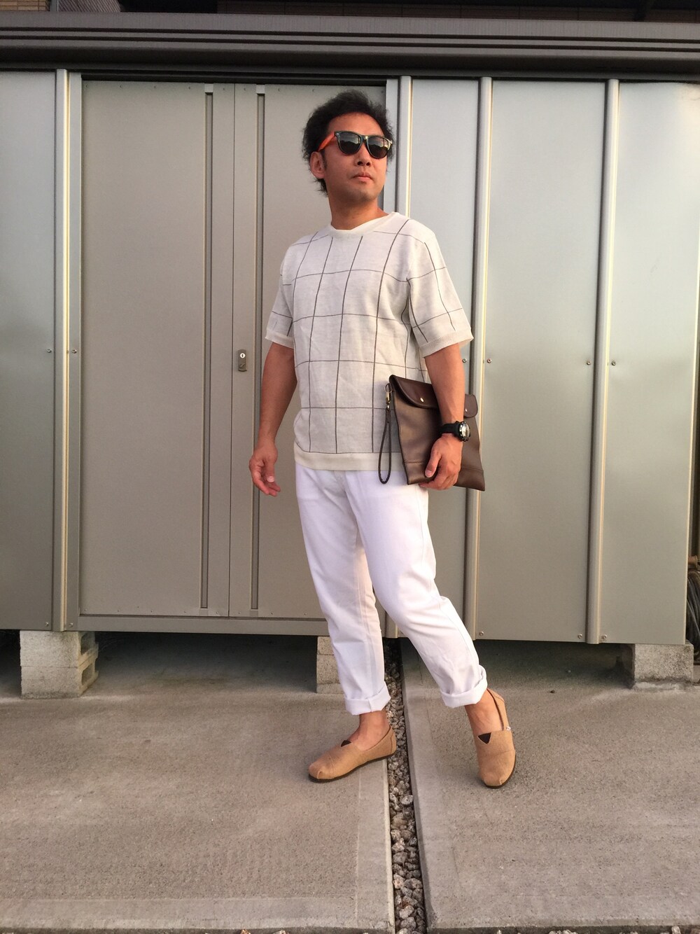 ホワイト系のニット/セーター、ブラウン系のクラッチバッグ、ホワイト系のチノパンツを着用したメンズの夏コーディネートの1枚目の写真