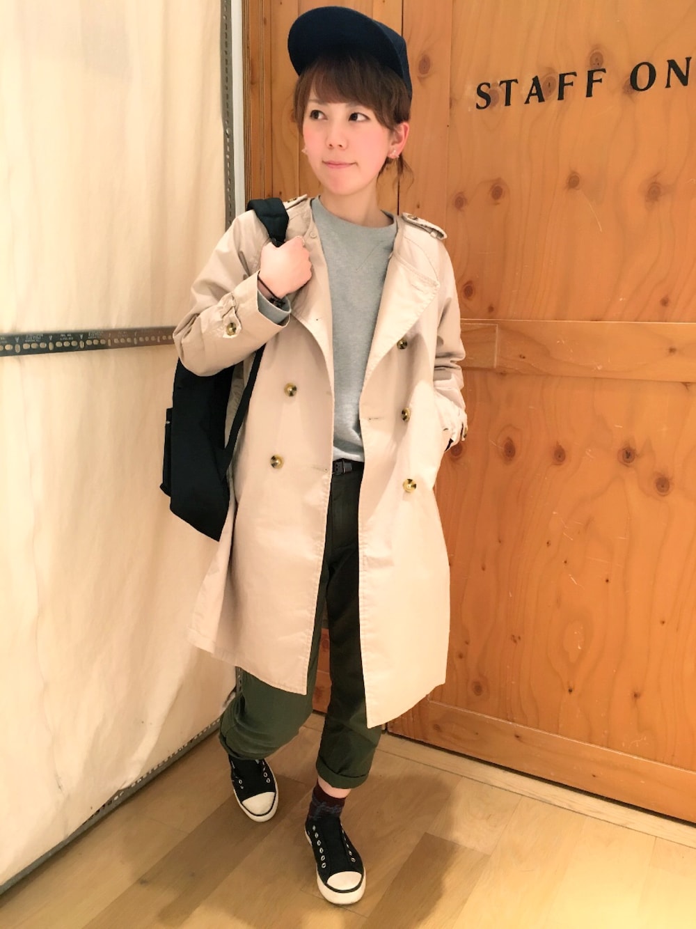 ベージュ系のトレンチコート、ブラック系のバックパック/リュック、グリーン系のチノパンツを着用したレディースの冬コーディネートの1枚目の写真