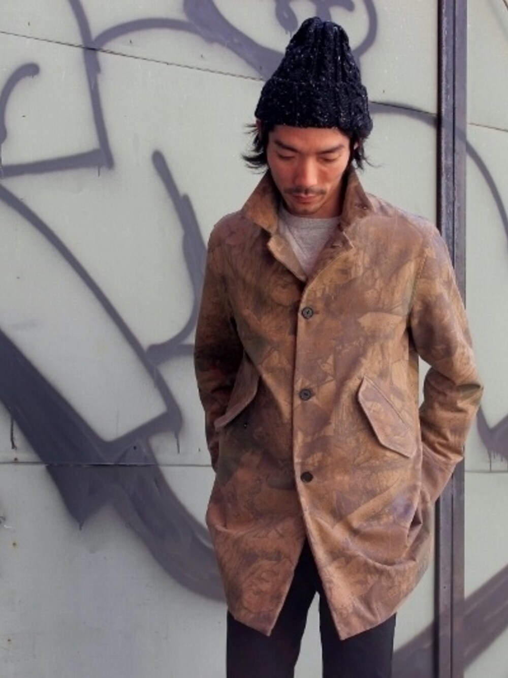 「ステンカラーコート、カモフラ、ニットキャップ、ハイランド2000、福岡」｜「AmanjakaniaのAmanjakaniaのオリジナルリーフカモ柄コート。
柄が馴染むようにウォッシュをかけて、古着に近い雰囲気。シルエットは妥協なくキレイです。
大人のおしゃれにどうでしょう！！（ステンカラーコート、ベージュ系）」を使った、HIDEOUTさん（メンズ・175cm）の秋コーディネートの1枚目の写真