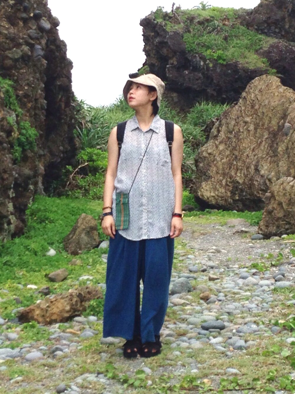 シルバー系のベスト、ブルー系のチノパンツ、グリーン系のバッグを着用したレディースの夏コーディネートの1枚目の写真