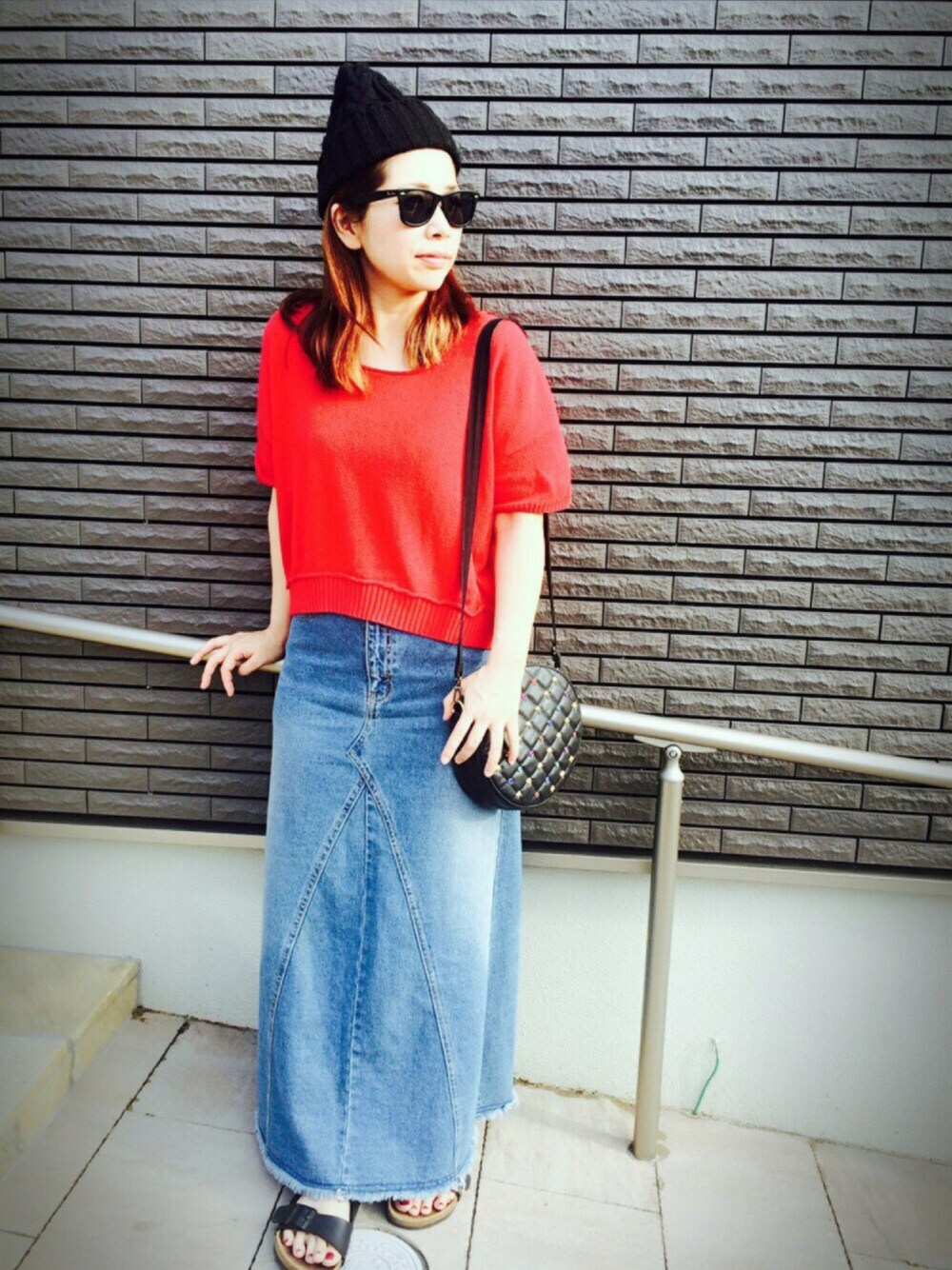 レッド系のニット/セーター、ブラック系のショルダーバッグ、ブルー系のデニムスカートを着用したレディースの夏コーディネートの1枚目の写真