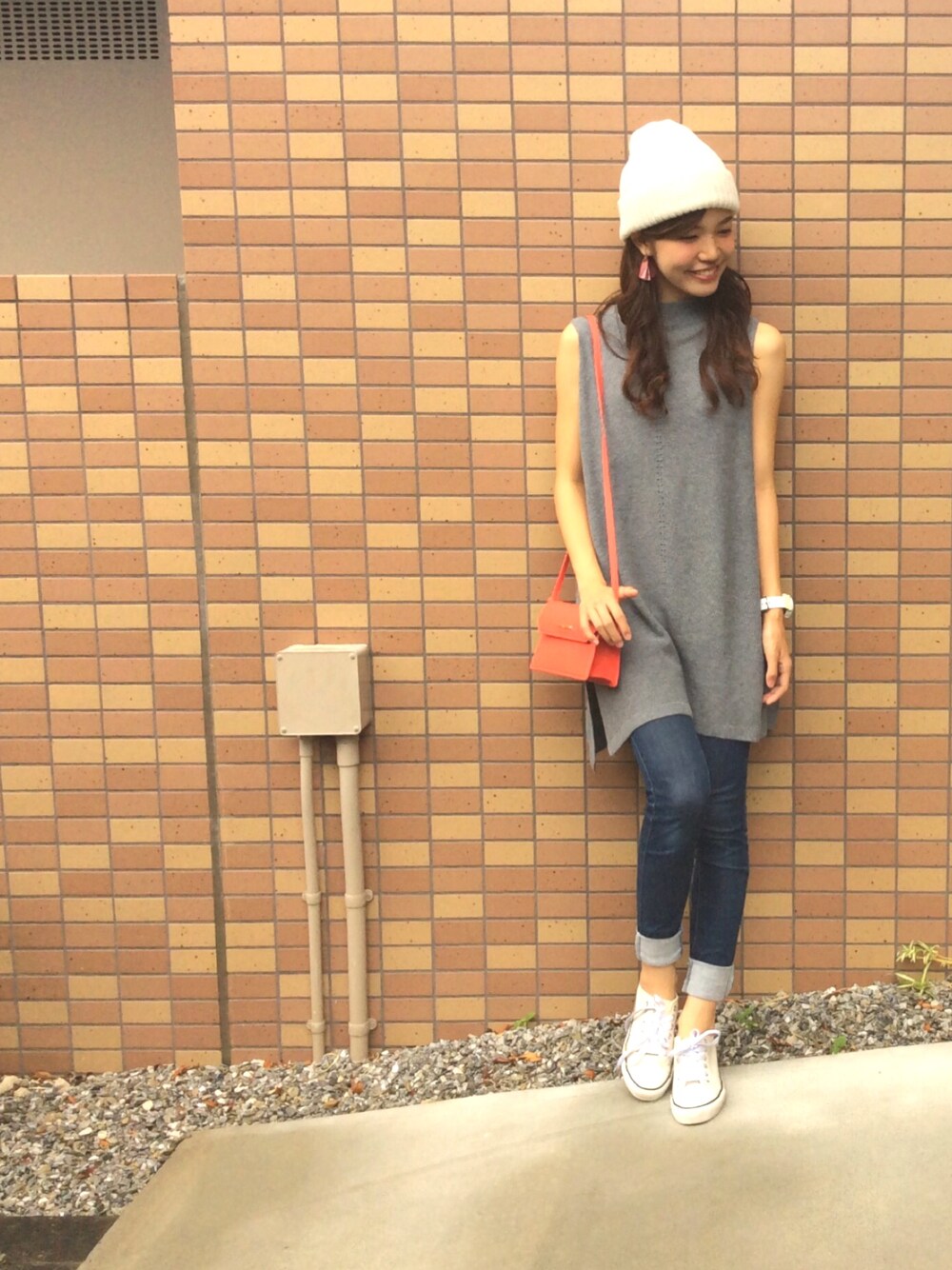 グレー系のニット/セーター、レッド系のショルダーバッグ、ブルー系のデニムパンツを着用したレディースの秋コーディネートの1枚目の写真