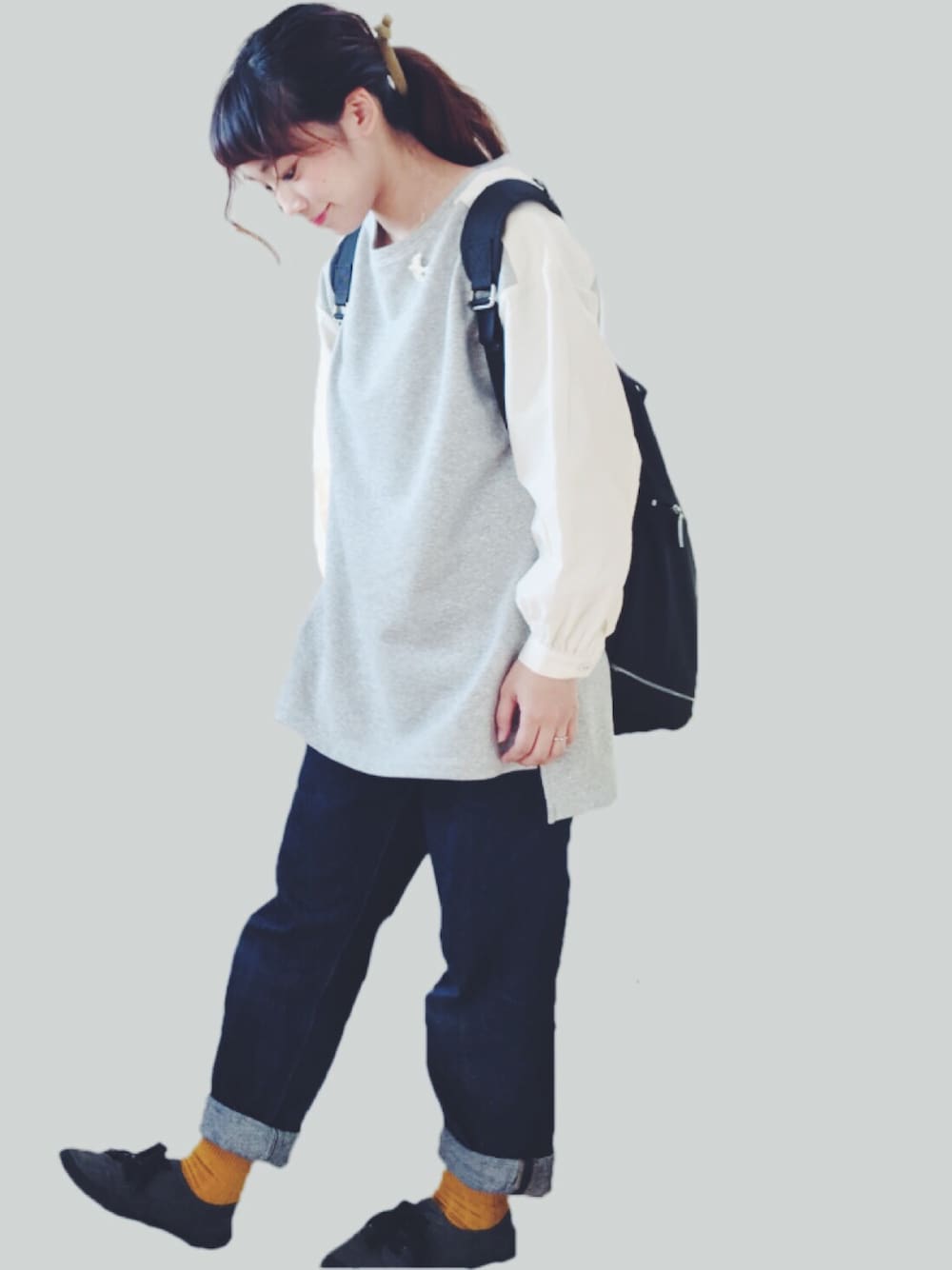 グレー系のチュニック、ブラック系のバックパック/リュック、ブルー系のデニムパンツを着用したレディースの秋コーディネートの1枚目の写真