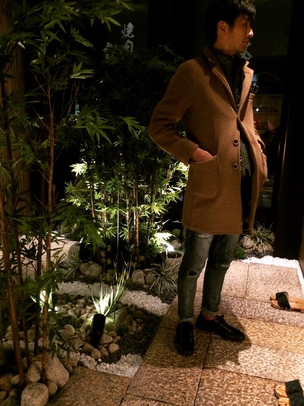 ベージュ系のチェスターコート、ブルー系のデニムパンツ、ブラック系のスニーカーを着用したメンズの秋コーディネートの1枚目の写真