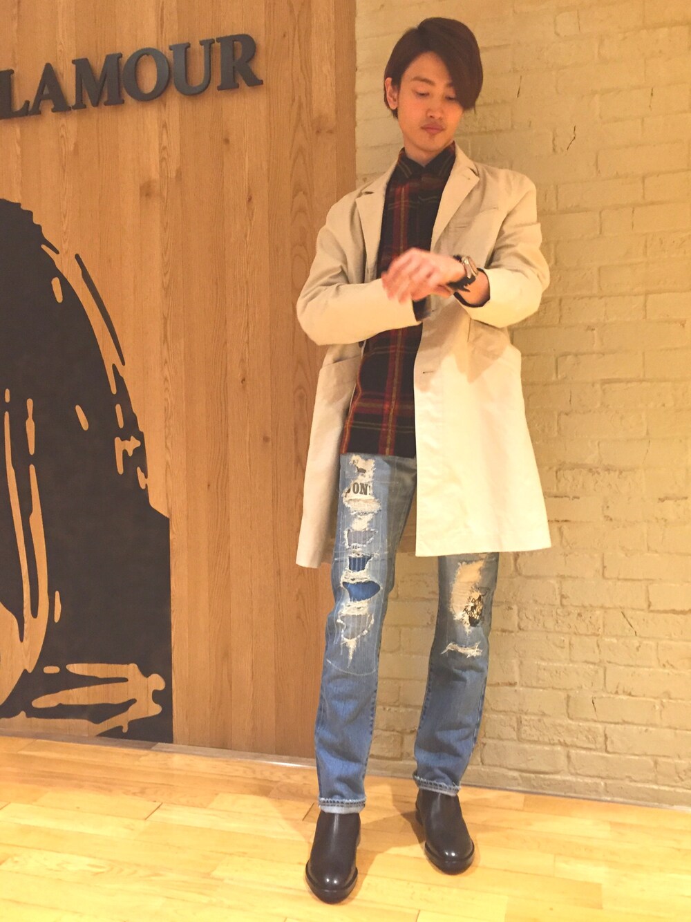 ブルー系のデニムパンツ、ベージュ系のチェスターコート、レッド系のポロシャツを着用したメンズの秋コーディネートの1枚目の写真