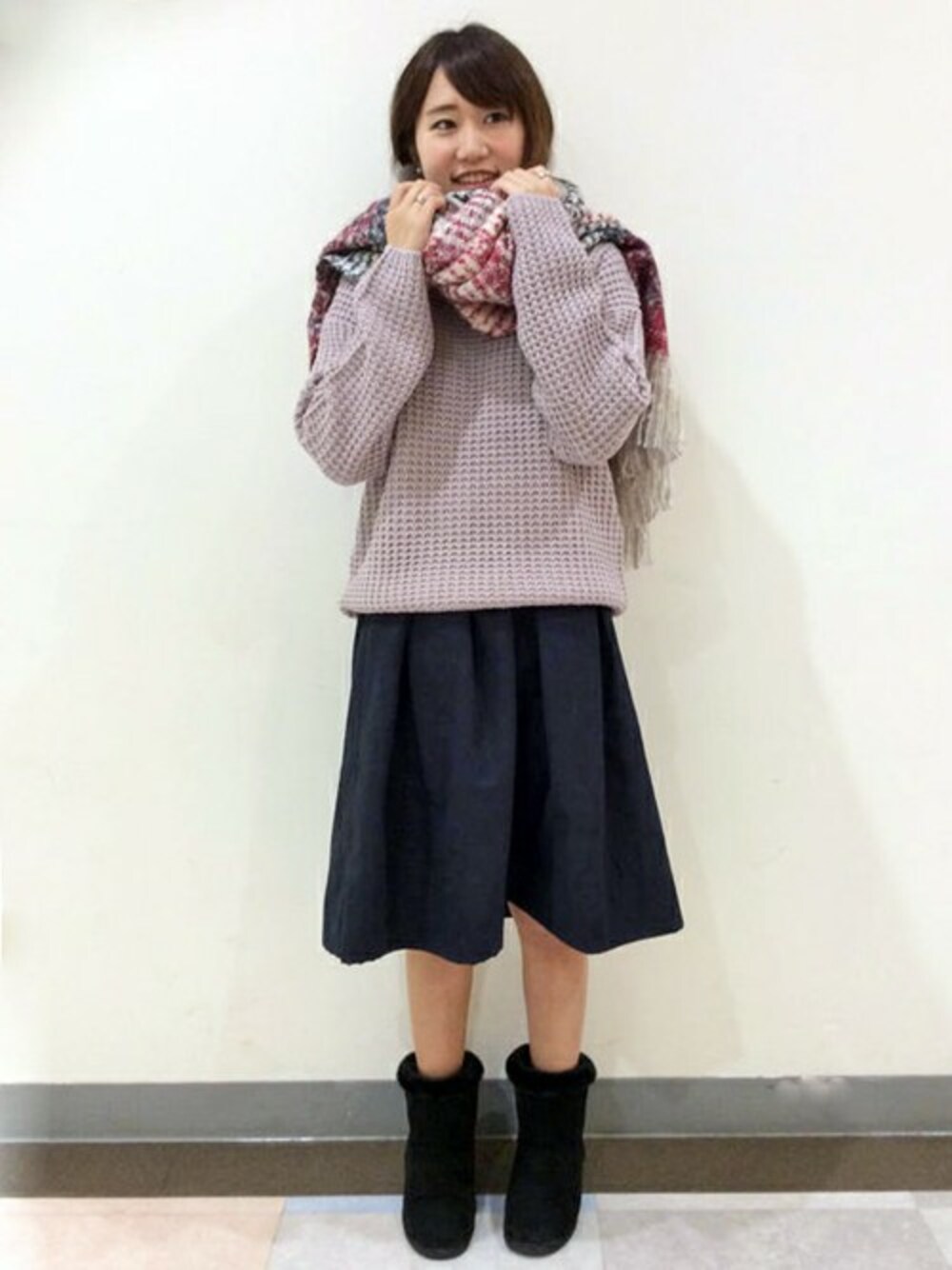 ピンク系のニット/セーター、グレー系のスカート、ブラック系のブーツを着用したレディースの冬コーディネートの1枚目の写真