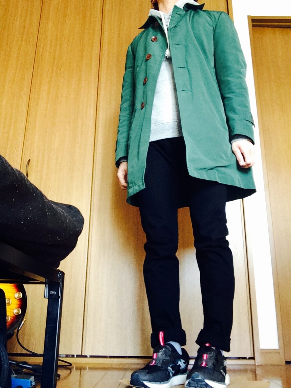 グリーン系のステンカラーコート、グレー系のTシャツ/カットソー、ブラック系のデニムパンツを着用したメンズの冬コーディネートの1枚目の写真