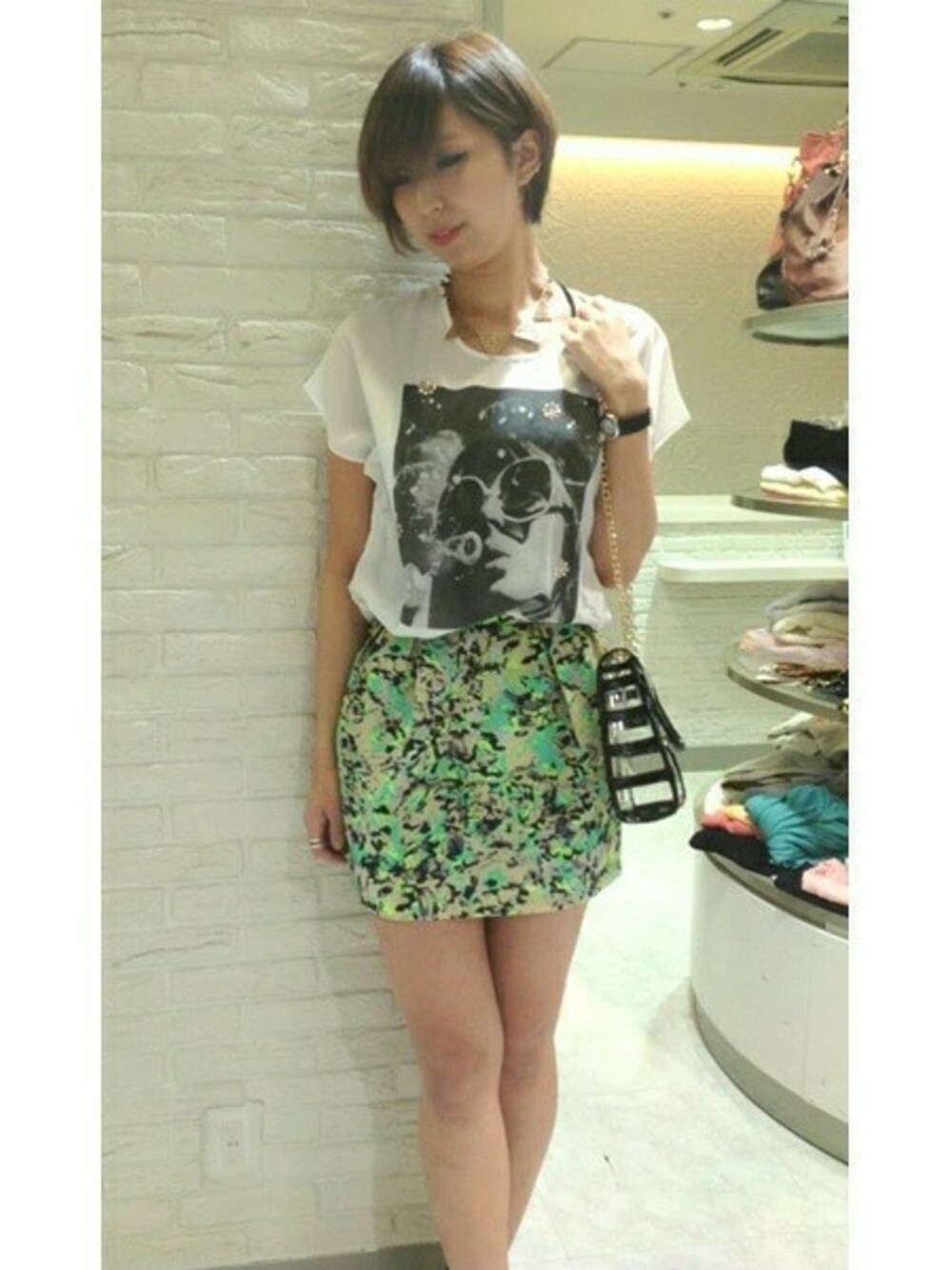 ブラック系のショルダーバッグ、ホワイト系のシャツ/ブラウス、グリーン系のスカートを着用したレディースの春コーディネートの1枚目の写真