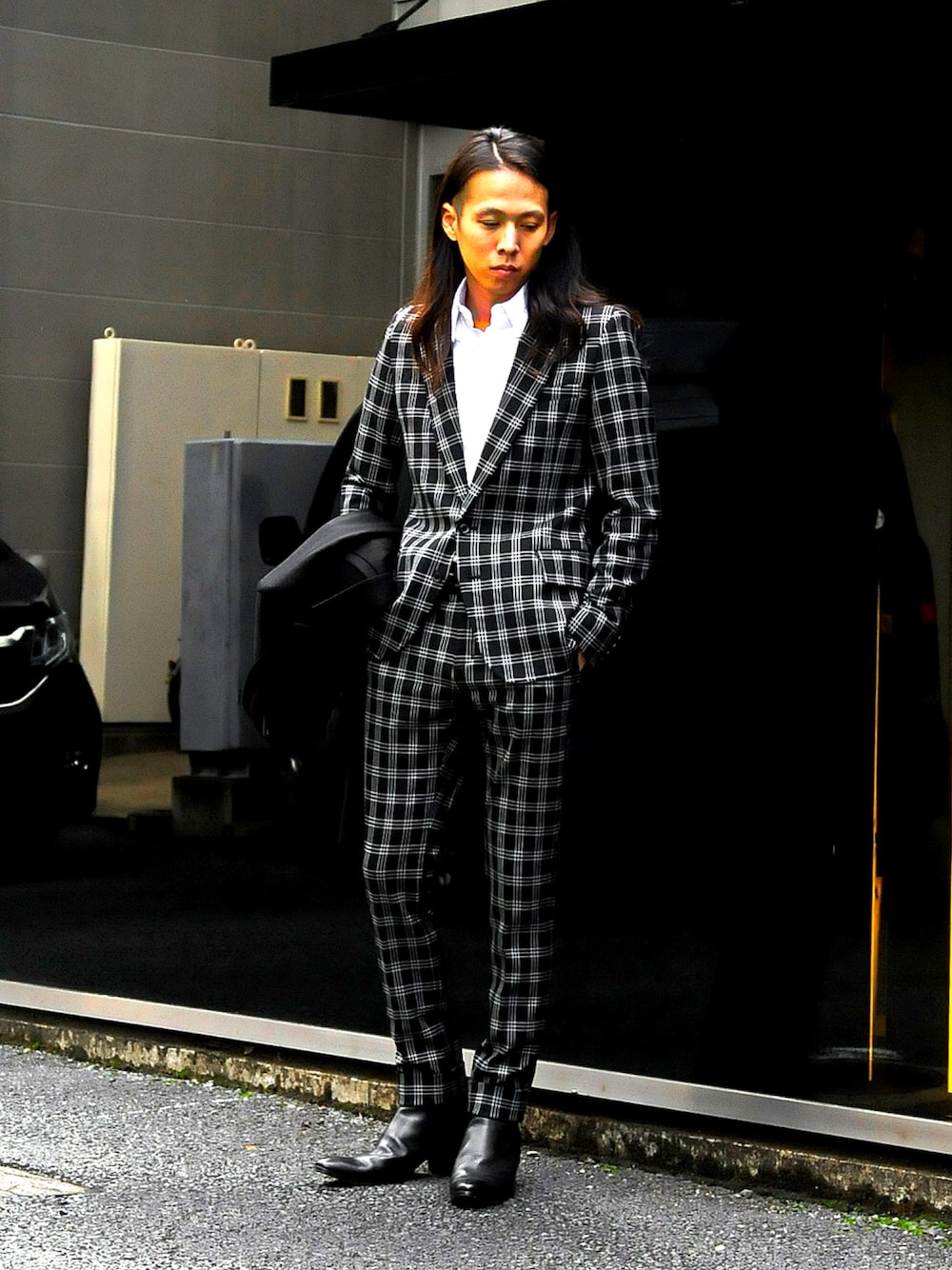 レッド系のテーラードジャケット、ブラック系のチェスターコート、ブラック系のブーツを着用したメンズの秋コーディネートの1枚目の写真