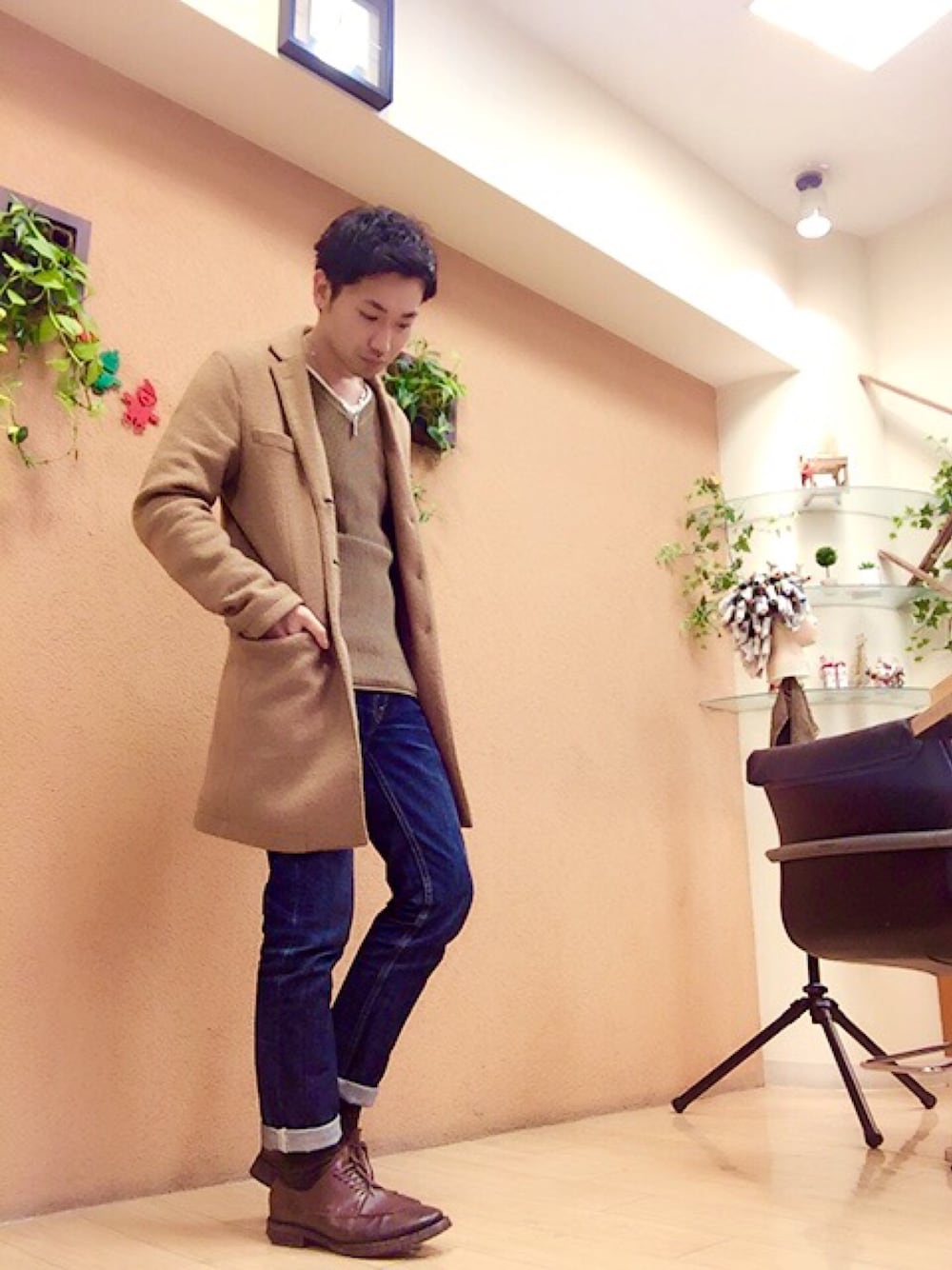 ベージュ系のチェスターコート、グリーン系のニット/セーター、ブルー系のデニムパンツを着用したメンズの秋コーディネートの1枚目の写真