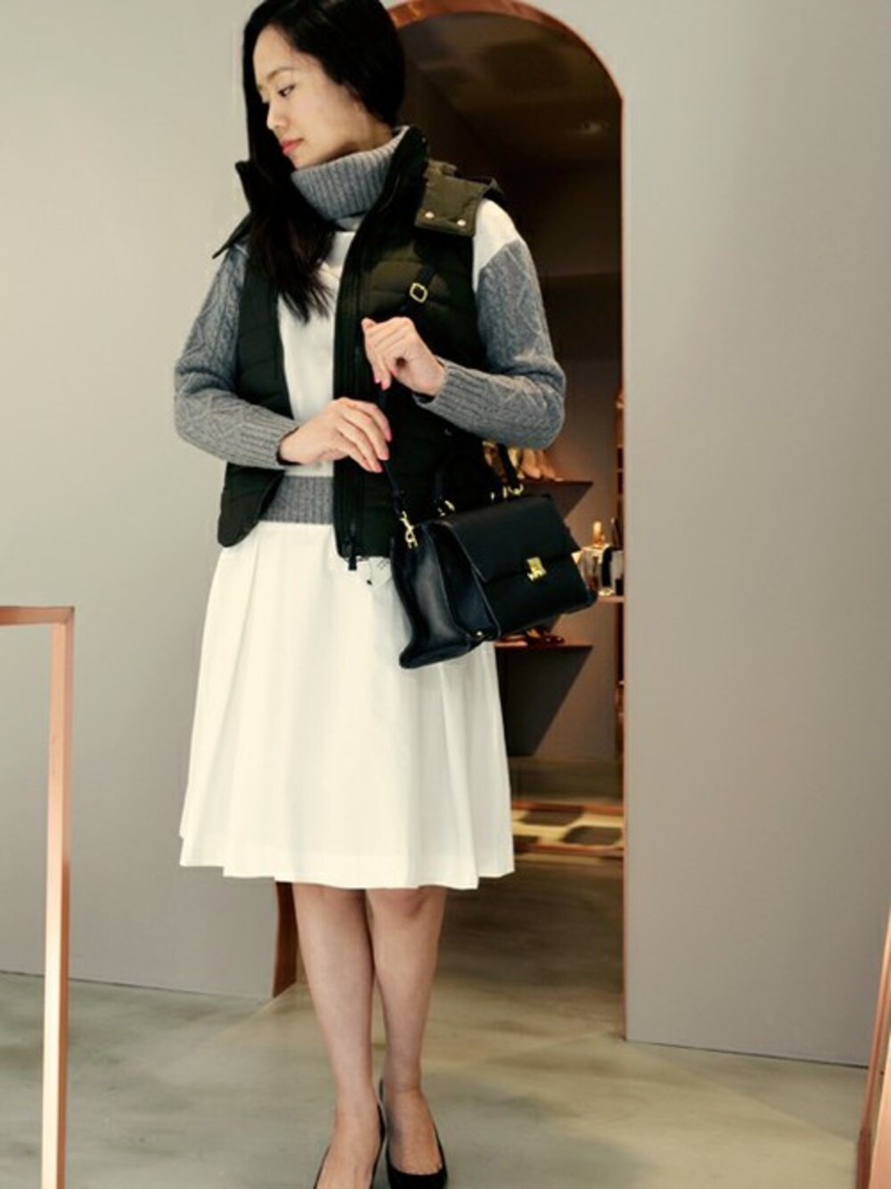 グリーン系のダウンベスト、ブラック系のショルダーバッグを着用したレディースの春コーディネートの1枚目の写真