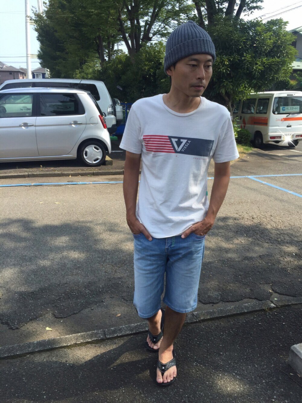 ベージュ系のTシャツ/カットソー、ブルー系のデニムパンツ、ブラック系のビーチサンダルを着用したメンズの夏コーディネートの1枚目の写真