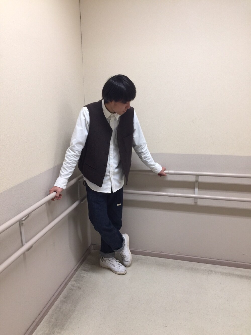 ブラウン系のベスト、ブルー系のデニムパンツ、ホワイト系のスニーカーを着用したメンズの秋コーディネートの1枚目の写真