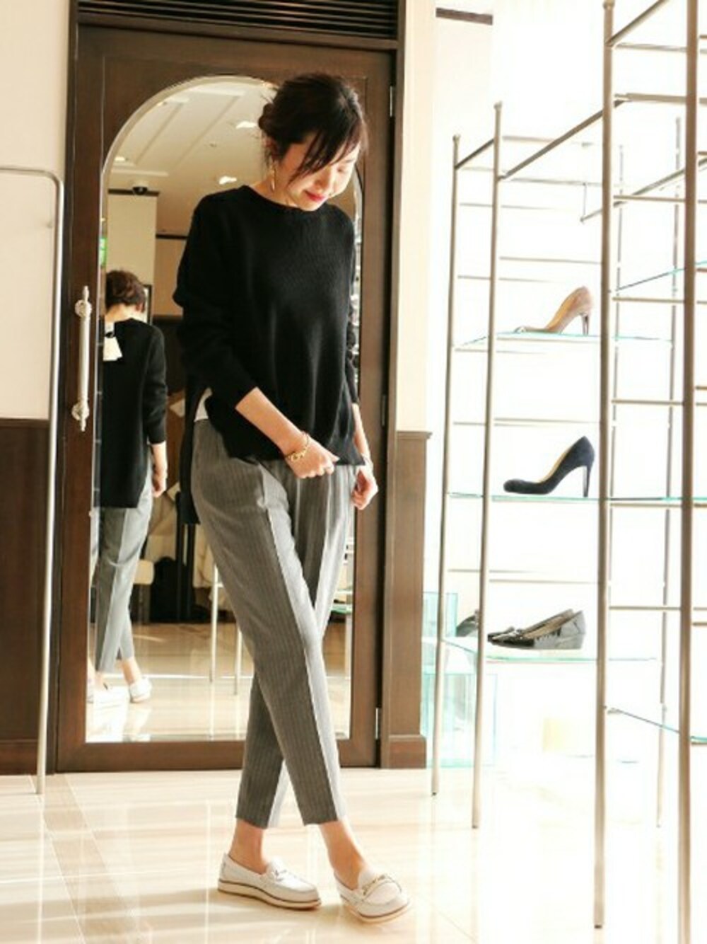 グレー系のその他パンツ、ブラック系のニット/セーター、ホワイト系のモカシン/デッキシューズを着用したレディースの春コーディネートの1枚目の写真