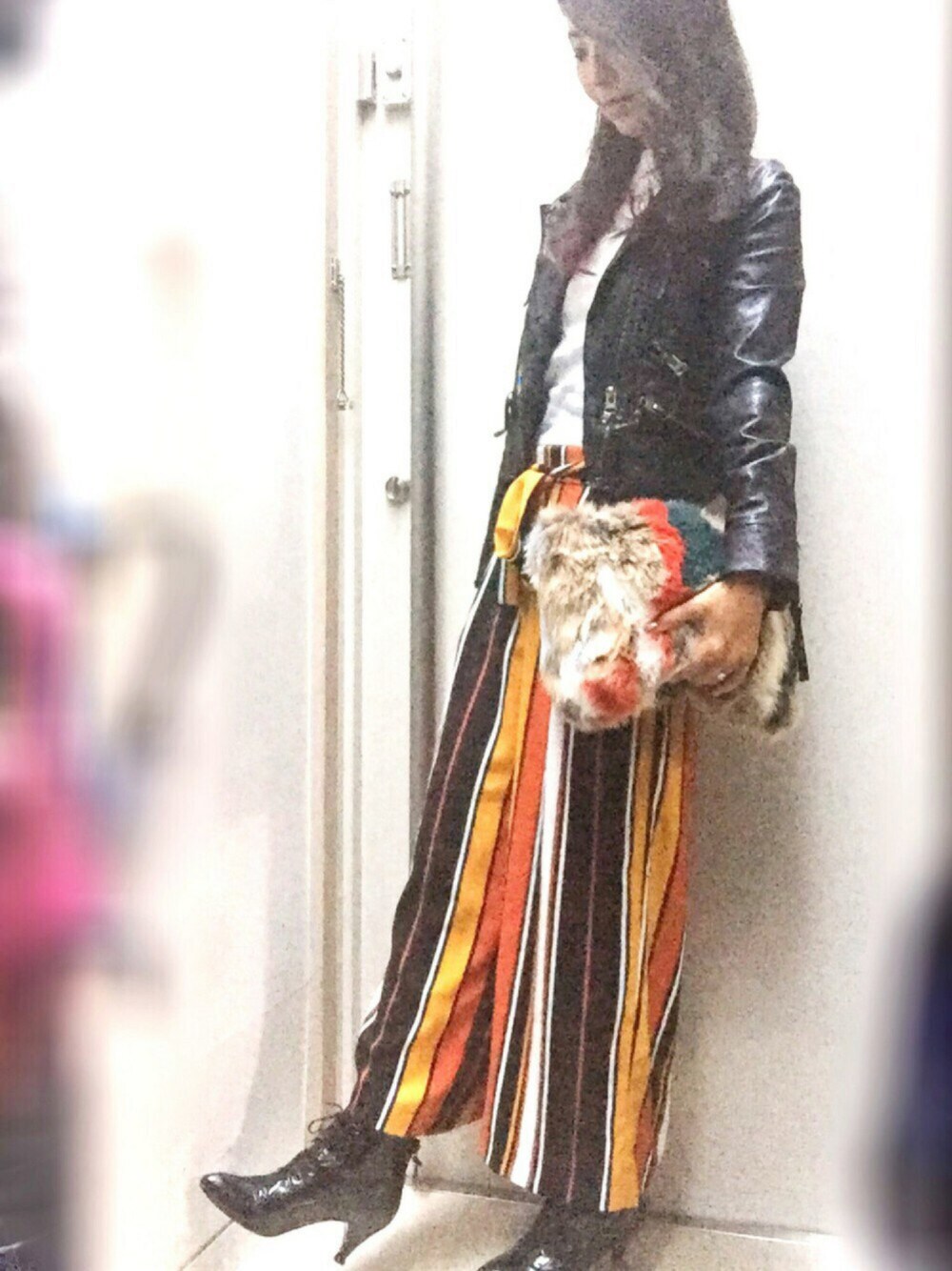 オレンジ系のパンツ、ブラック系のライダースジャケット、その他のクラッチバッグを着用したレディースの秋コーディネートの1枚目の写真