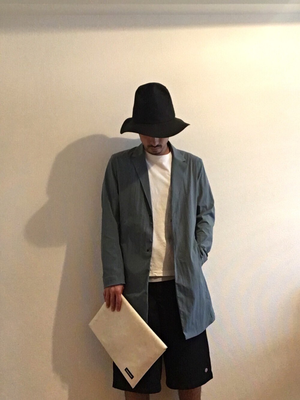 グリーン系のチェスターコート、ホワイト系のTシャツ/カットソー、ホワイト系のクラッチバッグを着用したメンズの春コーディネートの1枚目の写真