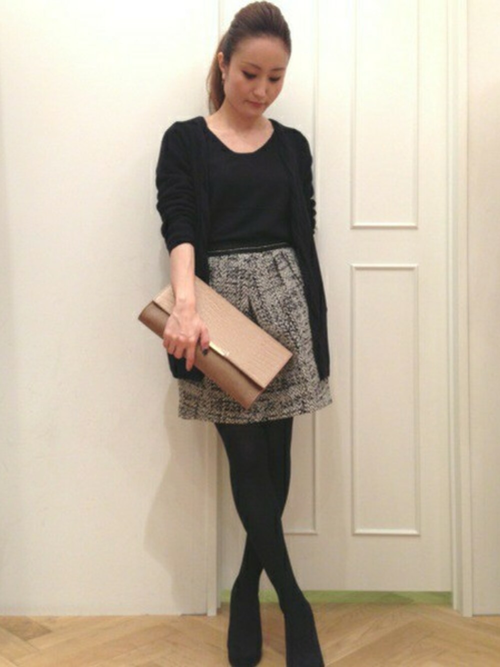 ブラック系のアンサンブル、ブラック系のスカート、ベージュ系のクラッチバッグを着用したレディースの秋コーディネートの1枚目の写真