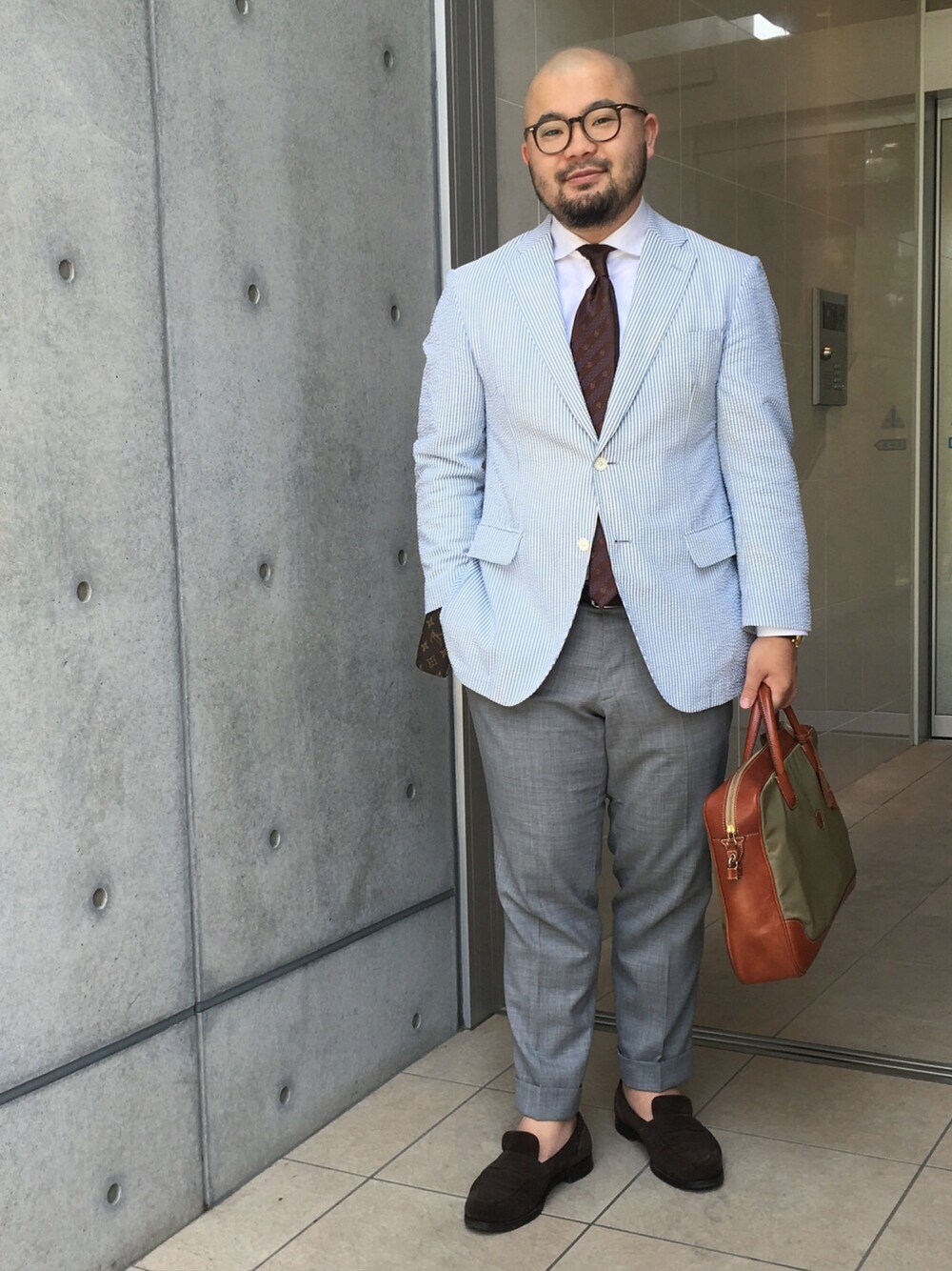 ブラウン系のネクタイ、ブラウン系のその他シューズ、グリーン系のビジネスバッグを着用したメンズの春コーディネートの1枚目の写真