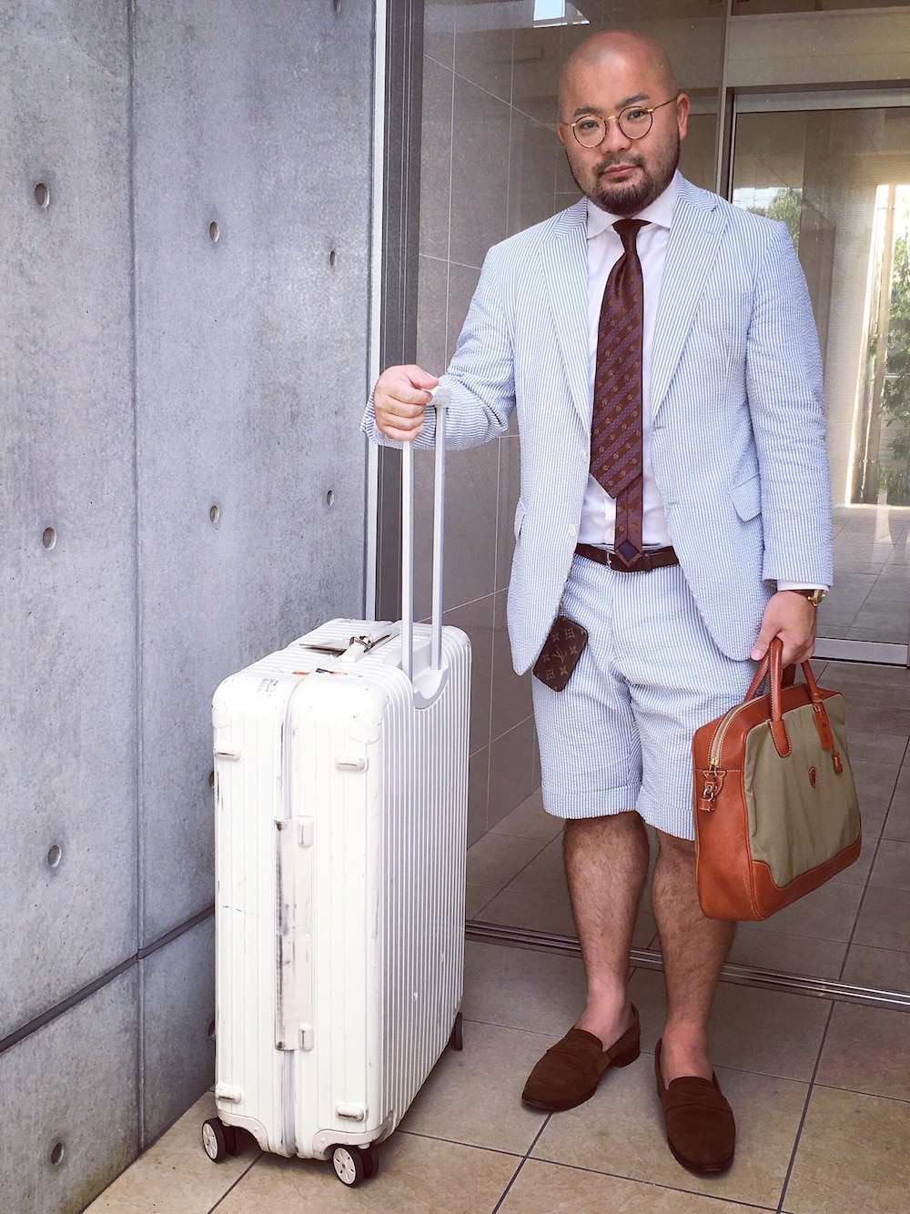 ブラウン系のネクタイ、ブラック系のスーツケース/キャリーバッグ、グリーン系のビジネスバッグを着用したメンズの夏コーディネートの1枚目の写真