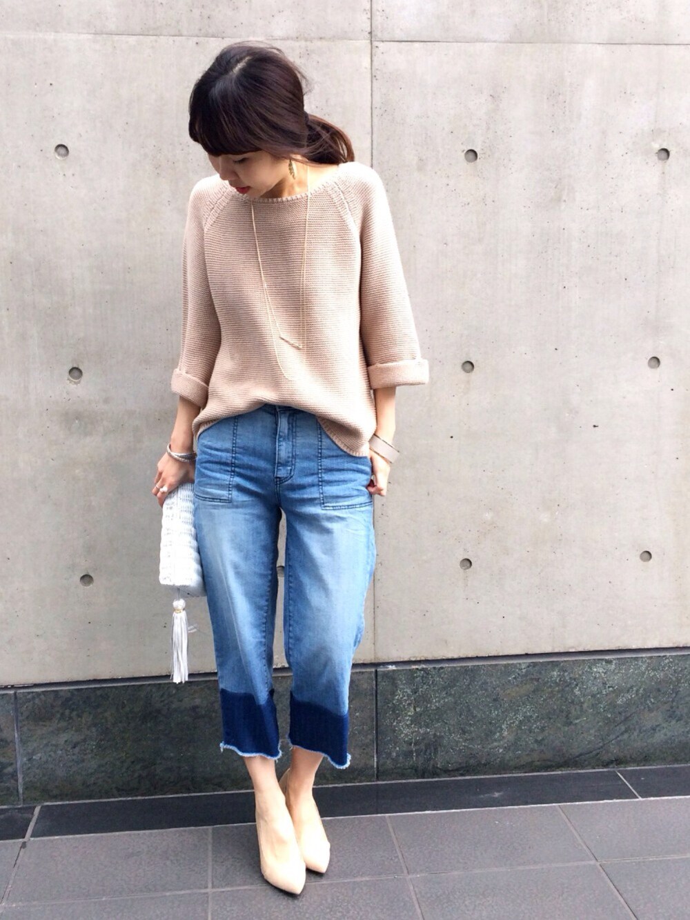 ベージュ系のニット/セーター、ホワイト系のクラッチバッグ、ブルー系のデニムパンツを着用したレディースの冬コーディネートの1枚目の写真