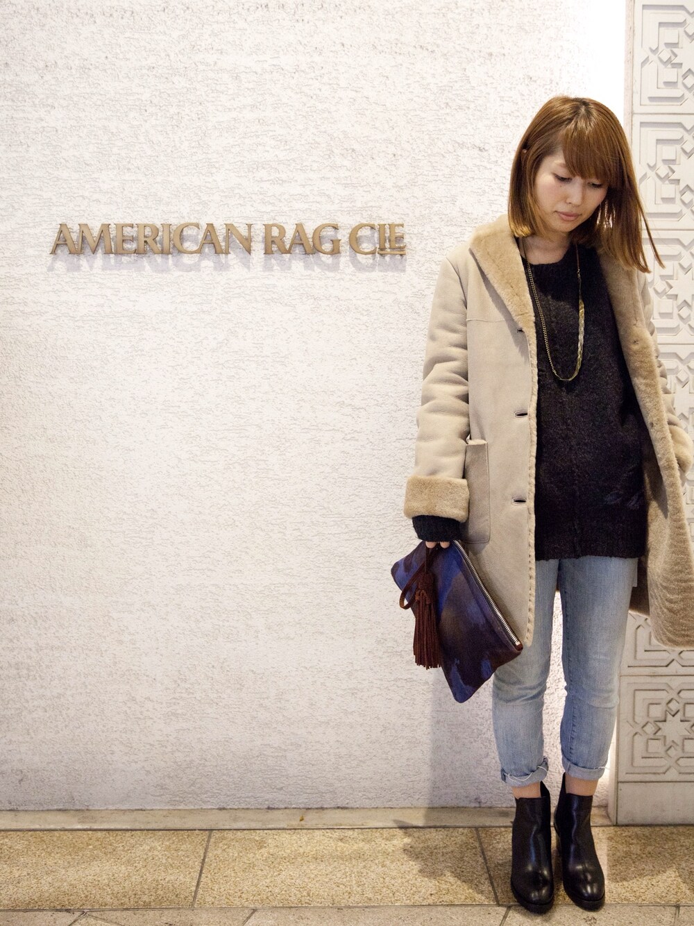 ベージュ系のムートンコート、ブラック系のブーツ、ブルー系のデニムパンツを着用したレディースの冬コーディネートの1枚目の写真