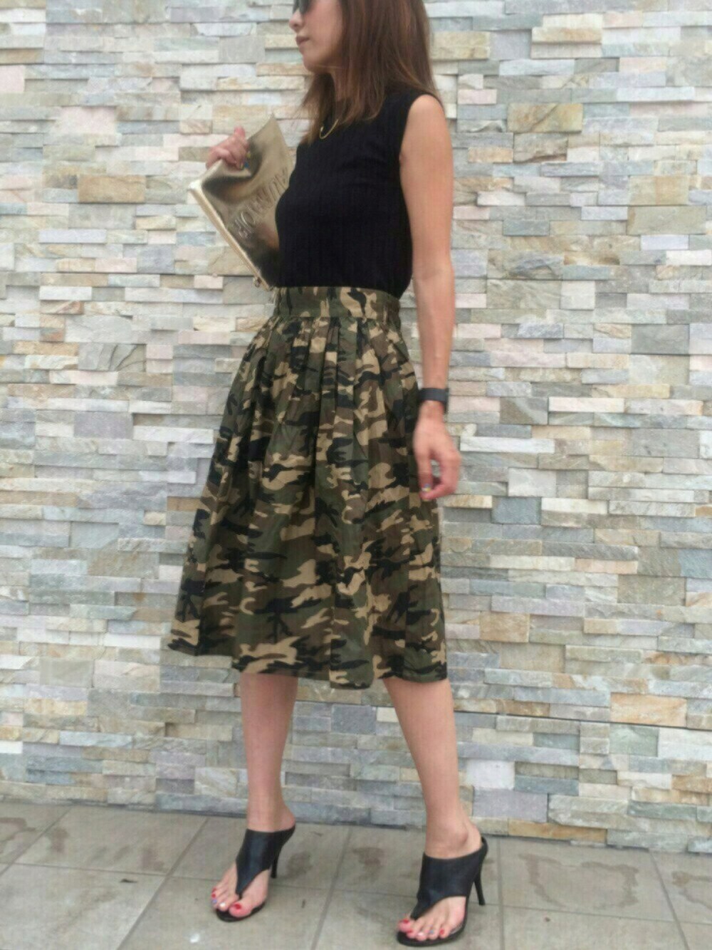 ブラック系のサンダル、ゴールド系のクラッチバッグ、グリーン系のスカートを着用したレディースの夏コーディネートの1枚目の写真