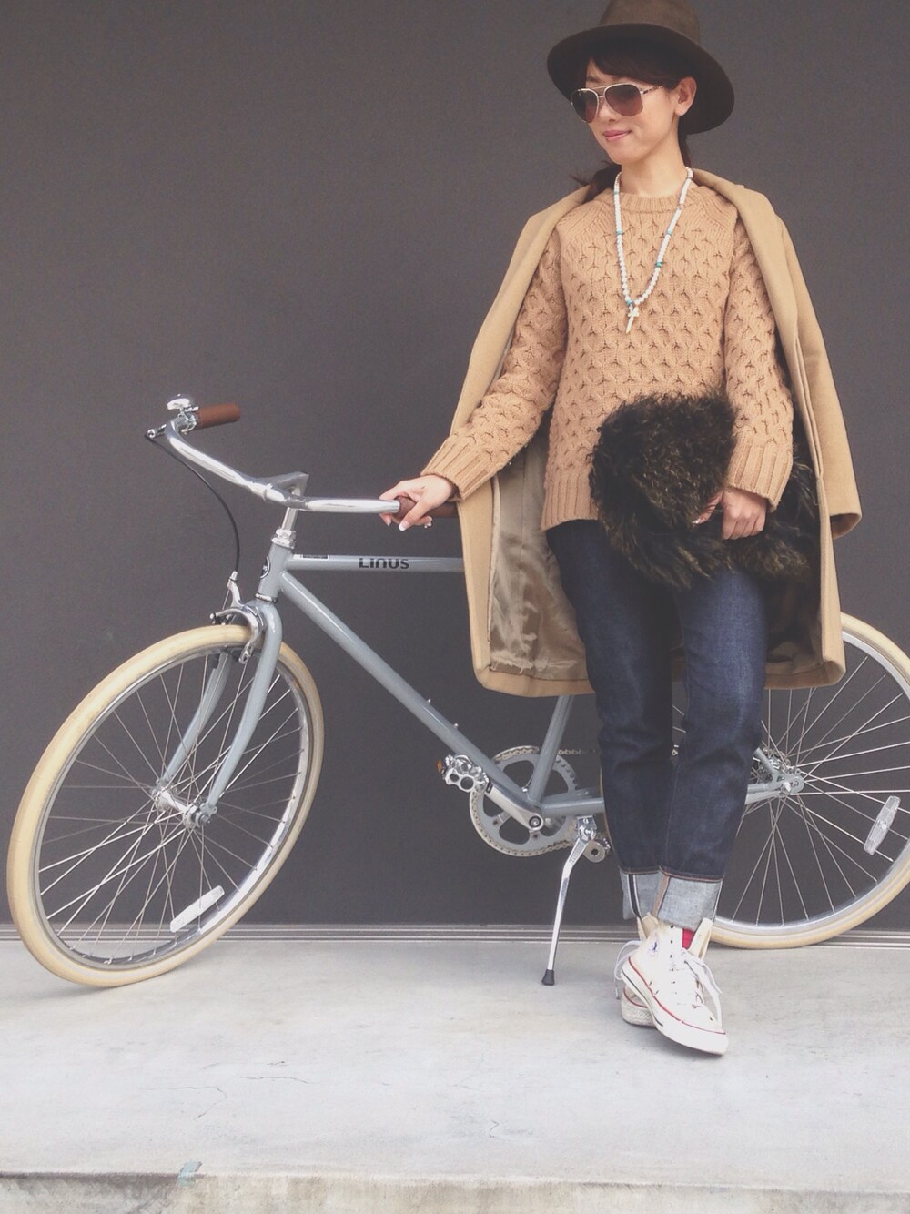 ベージュ系のニット/セーター、ブルー系のデニムパンツ、グリーン系のクラッチバッグを着用したレディースの冬コーディネートの1枚目の写真