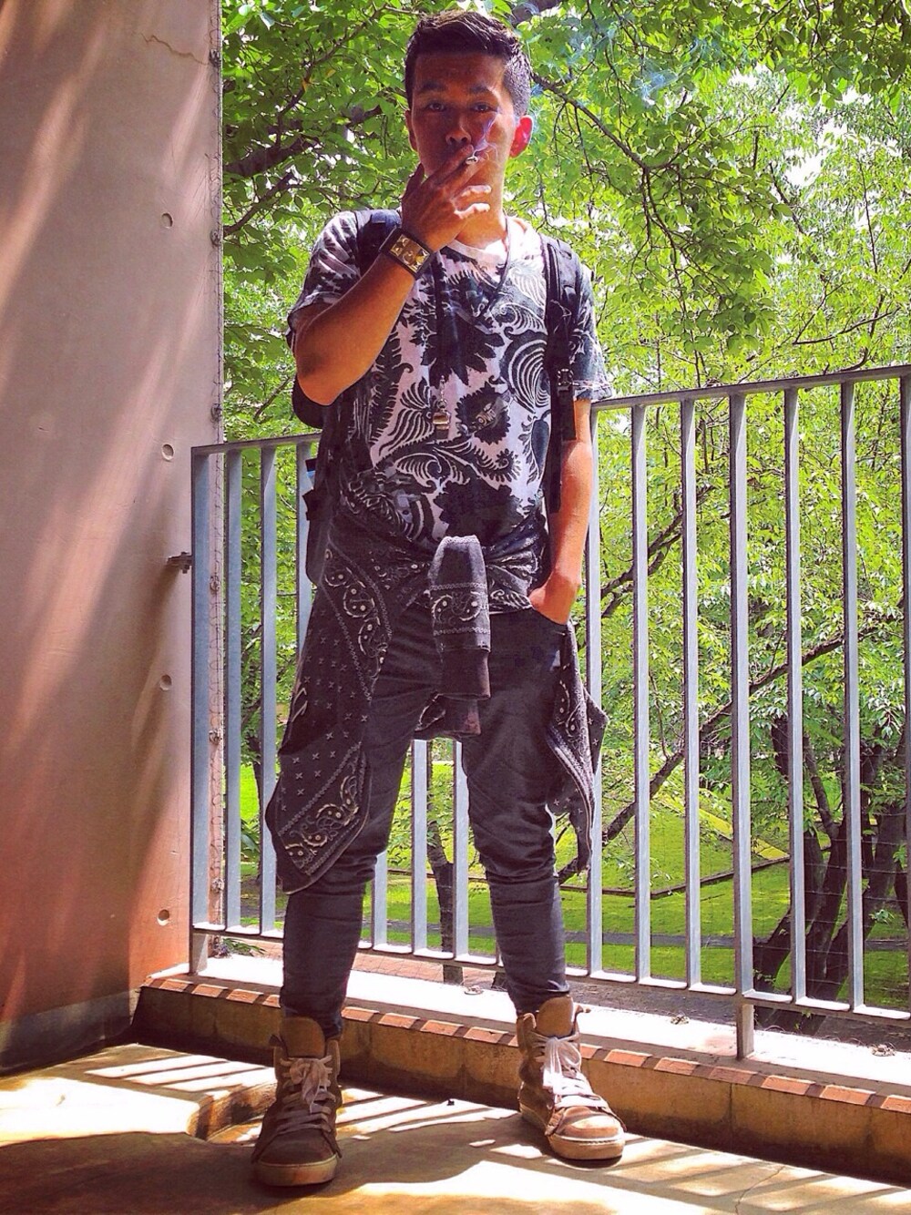 ブラック系のショルダーバッグ、グリーン系のTシャツ/カットソー、ベージュ系のスニーカーを着用したメンズの夏コーディネートの1枚目の写真