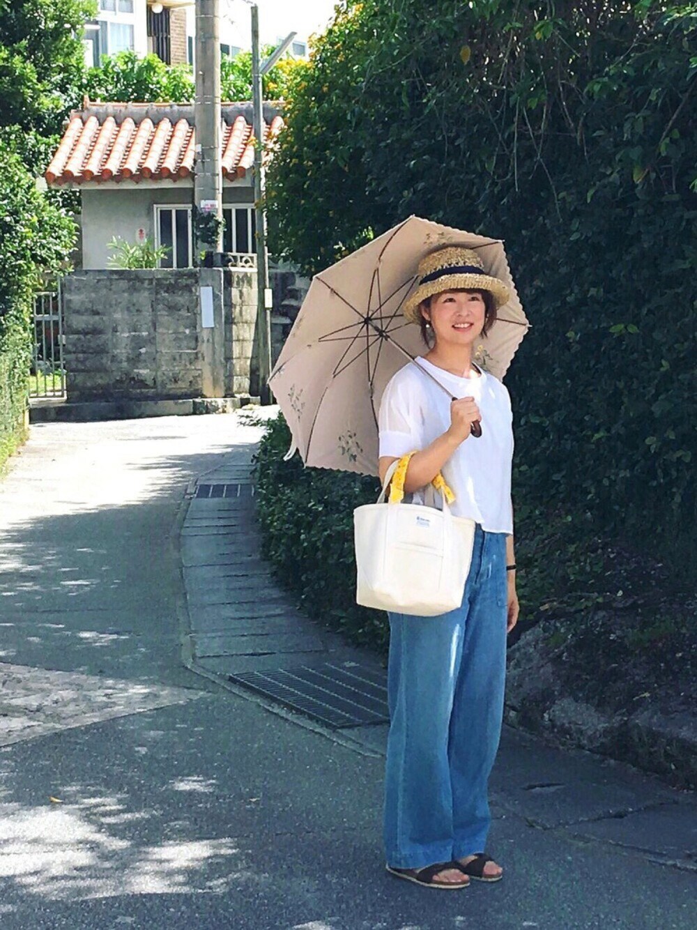 ホワイト系のトートバッグ、ホワイト系のTシャツ/カットソー、ブラウン系のサンダルを着用したレディースの夏コーディネートの1枚目の写真