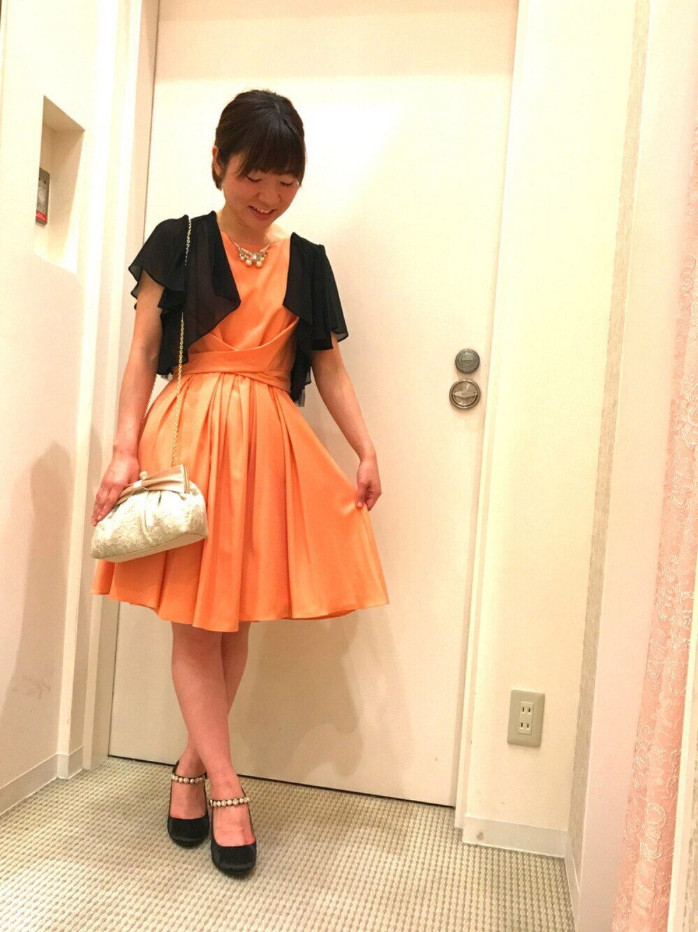 オレンジ系のドレス、ベージュ系のクラッチバッグ、ブラック系のパンプスを着用したレディースの秋コーディネートの1枚目の写真